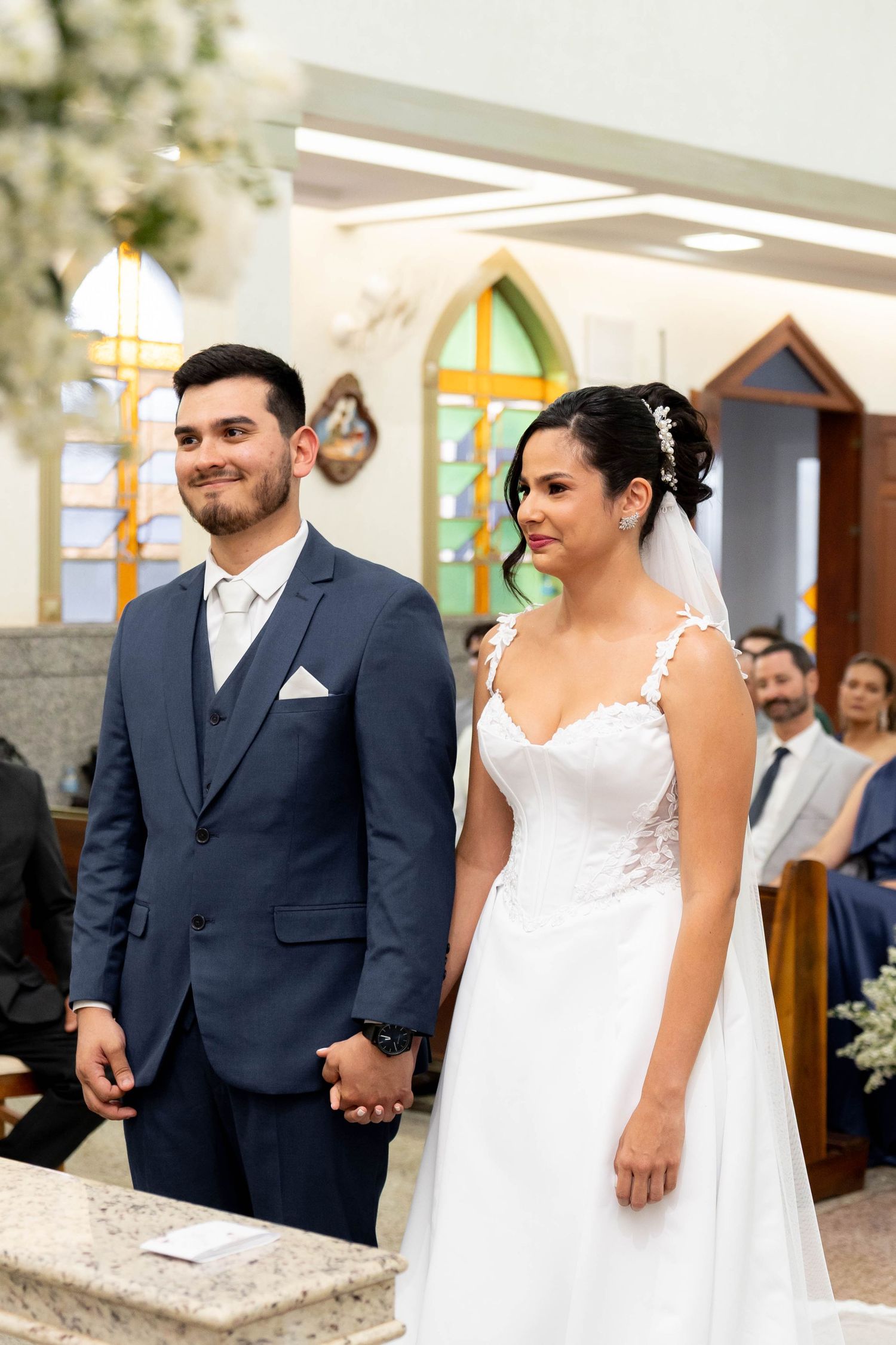 A smiling bride and groom hold hands at the altar during their church wedding ceremony.
