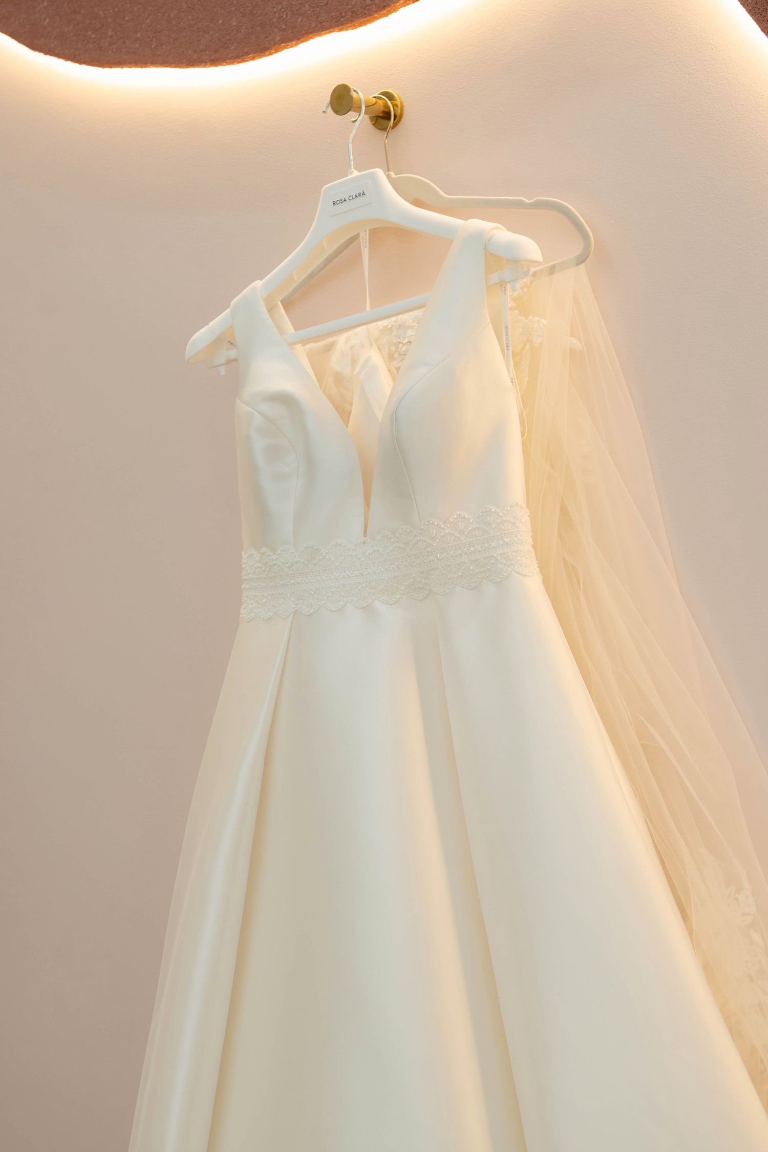 Elegant white A-line wedding dress with lace waist detail and veil hanging on a white hanger.