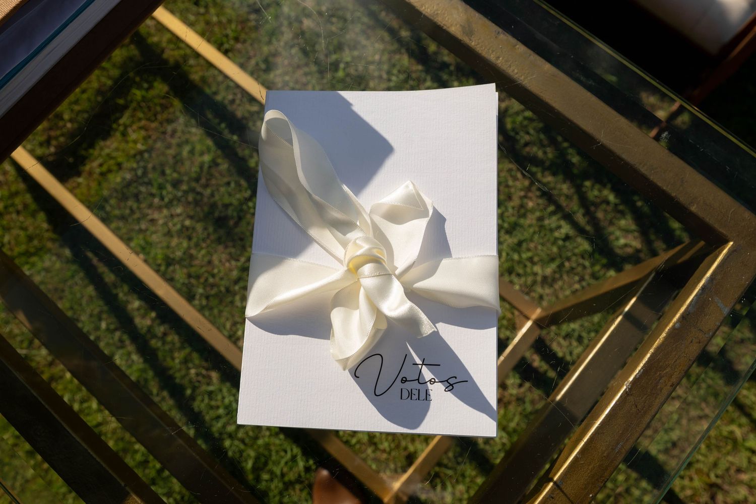 White gift card with cream satin bow on gold glass table, featuring elegant Vuitton signature branding.