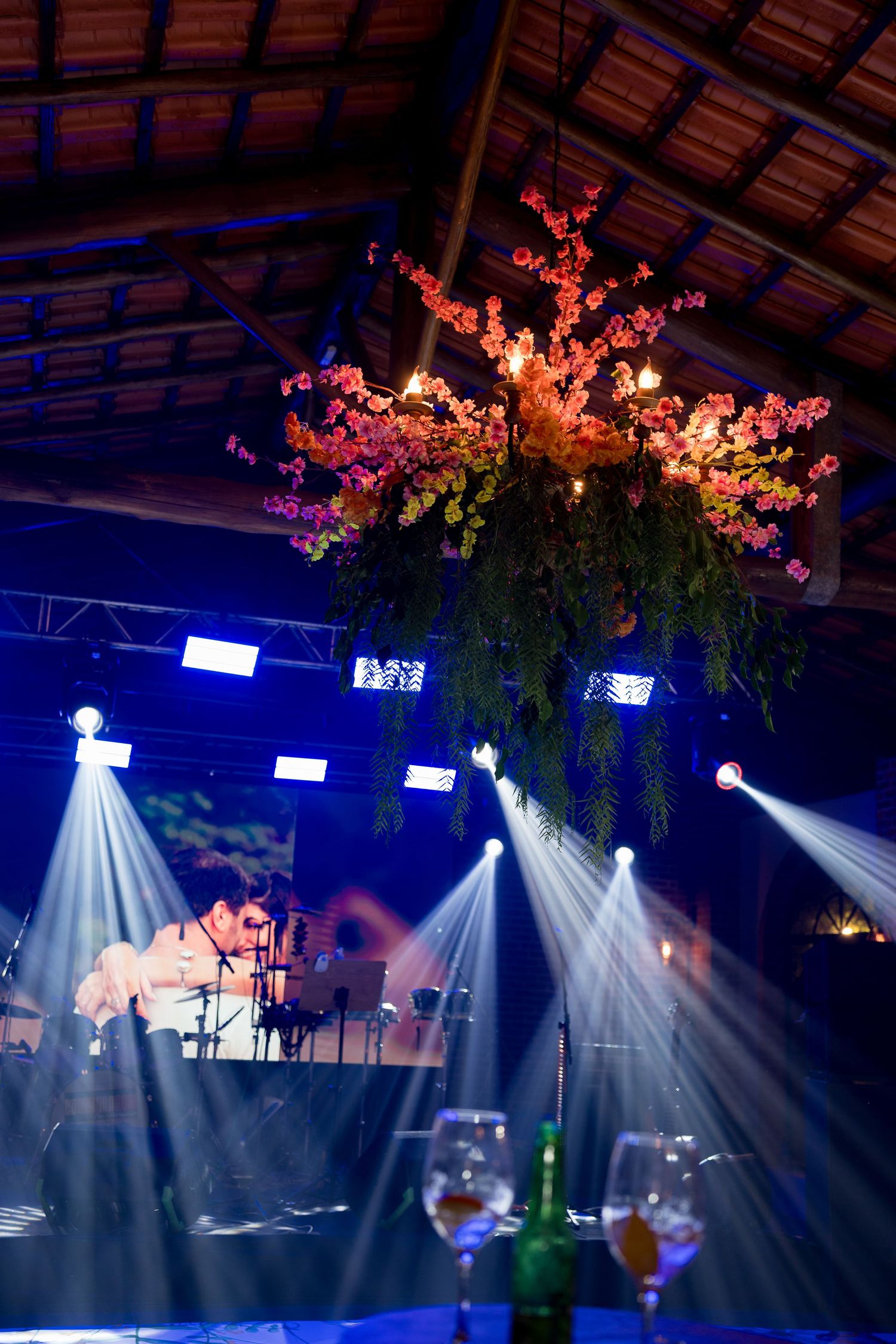 Elegant event venue with hanging floral centerpiece, blue stage lights, and live musician performing in background.