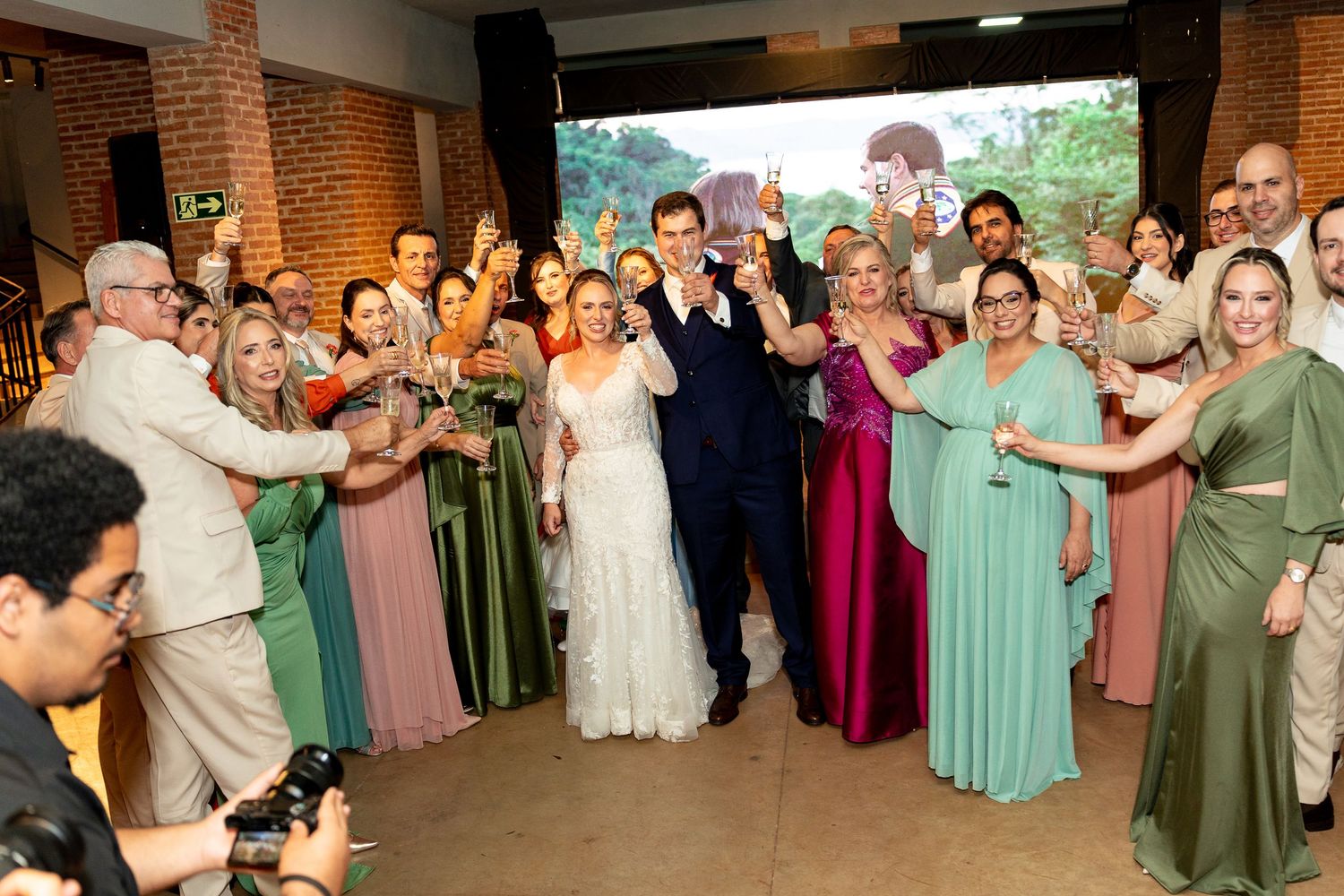 Bride and groom celebrate with wedding party and guests raising glasses in a toast at a elegant indoor wedding reception.