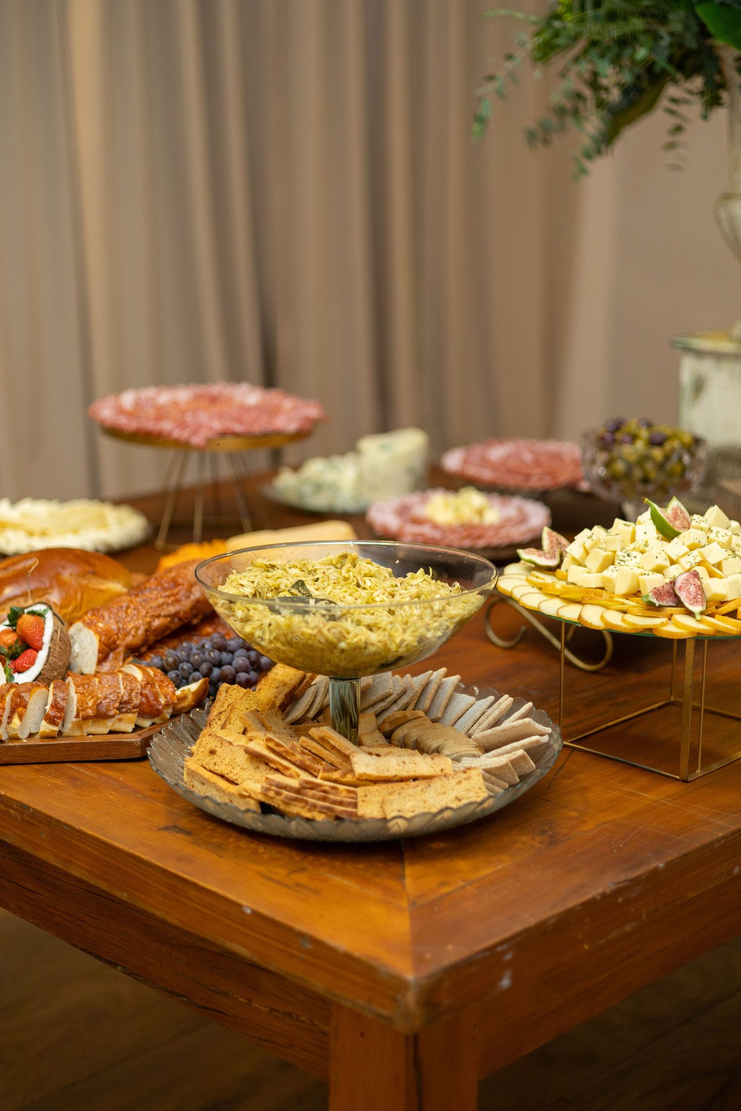 Elegant charcuterie and appetizer spread on a wooden table featuring crackers, cheese, meats, and fresh fruit at a catered event.