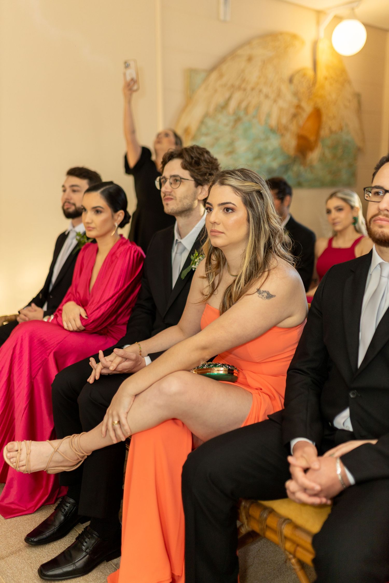 Wedding guests in formal attire seated during a ceremony, woman in orange dress.
