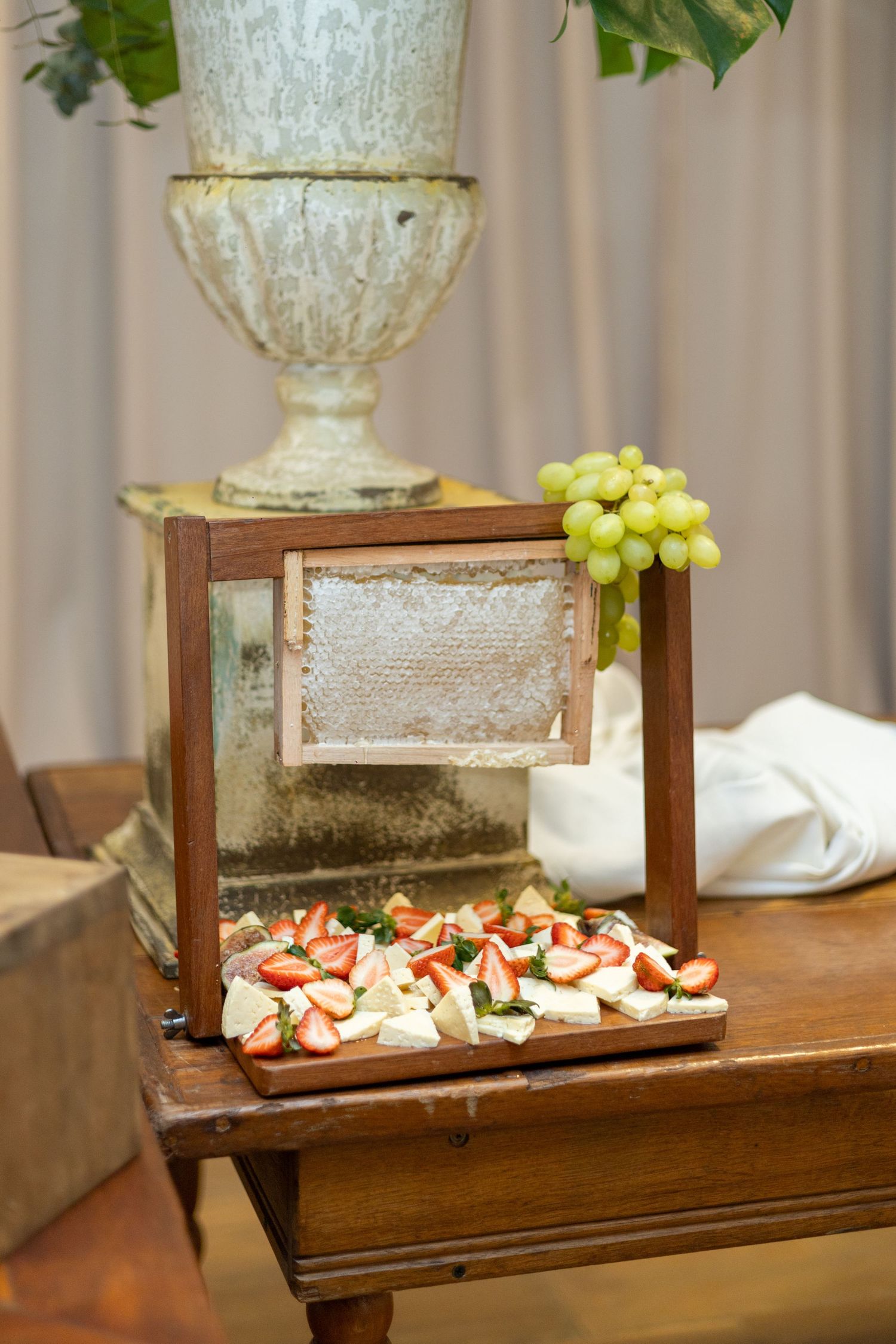 Elegant charcuterie board with strawberries and cheese beside honeycomb frame with green grapes on rustic wooden table.