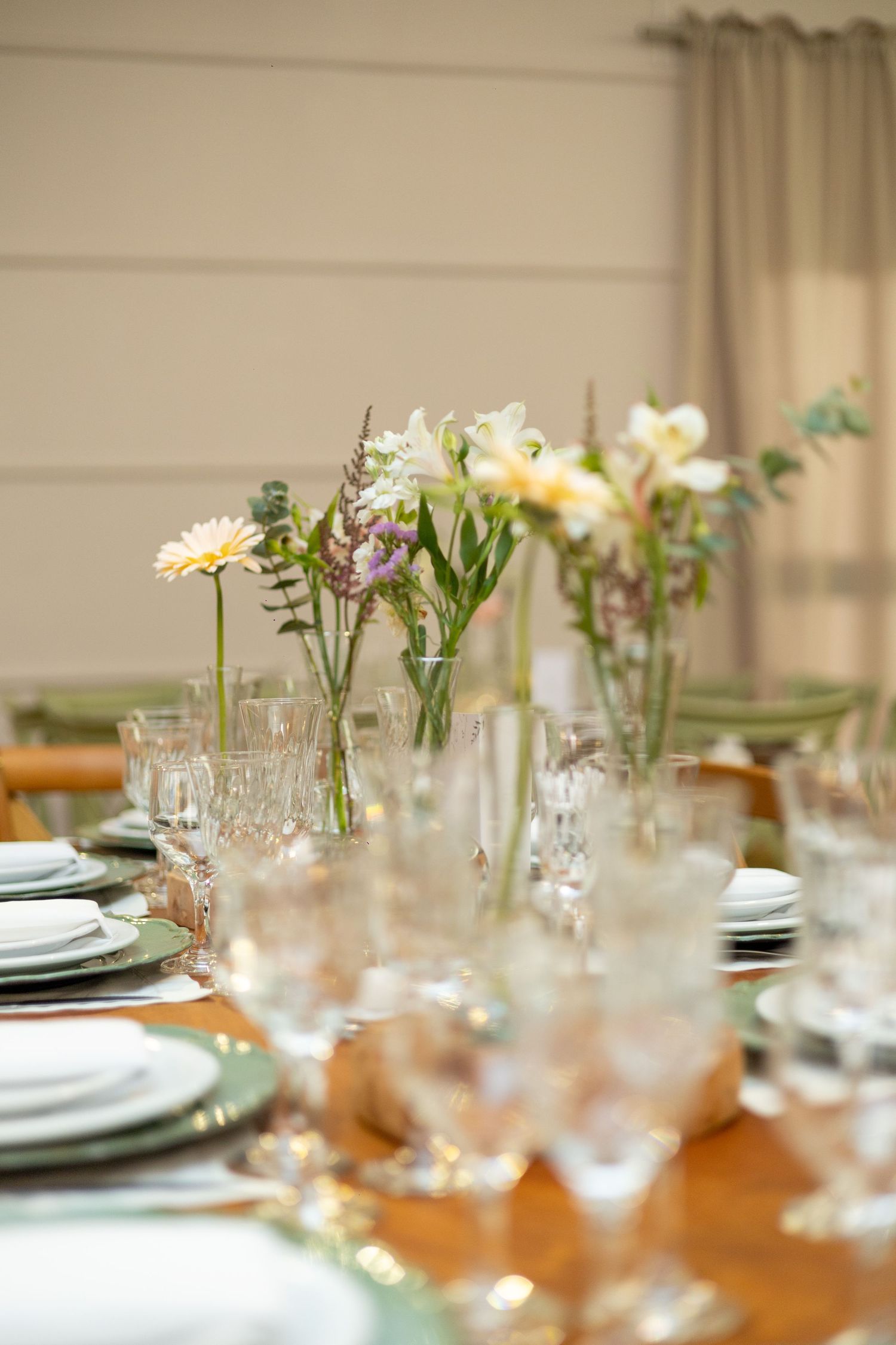 Elegant dining table set with crystal glasses, white plates, and fresh spring flower arrangements in glass vases.