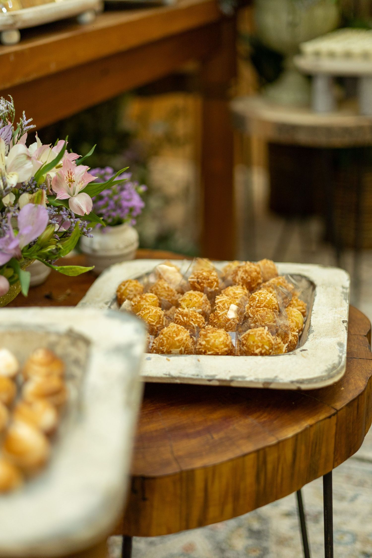 Rustic wedding dessert table with golden coconut truffles on a white tray beside fresh purple flowers.