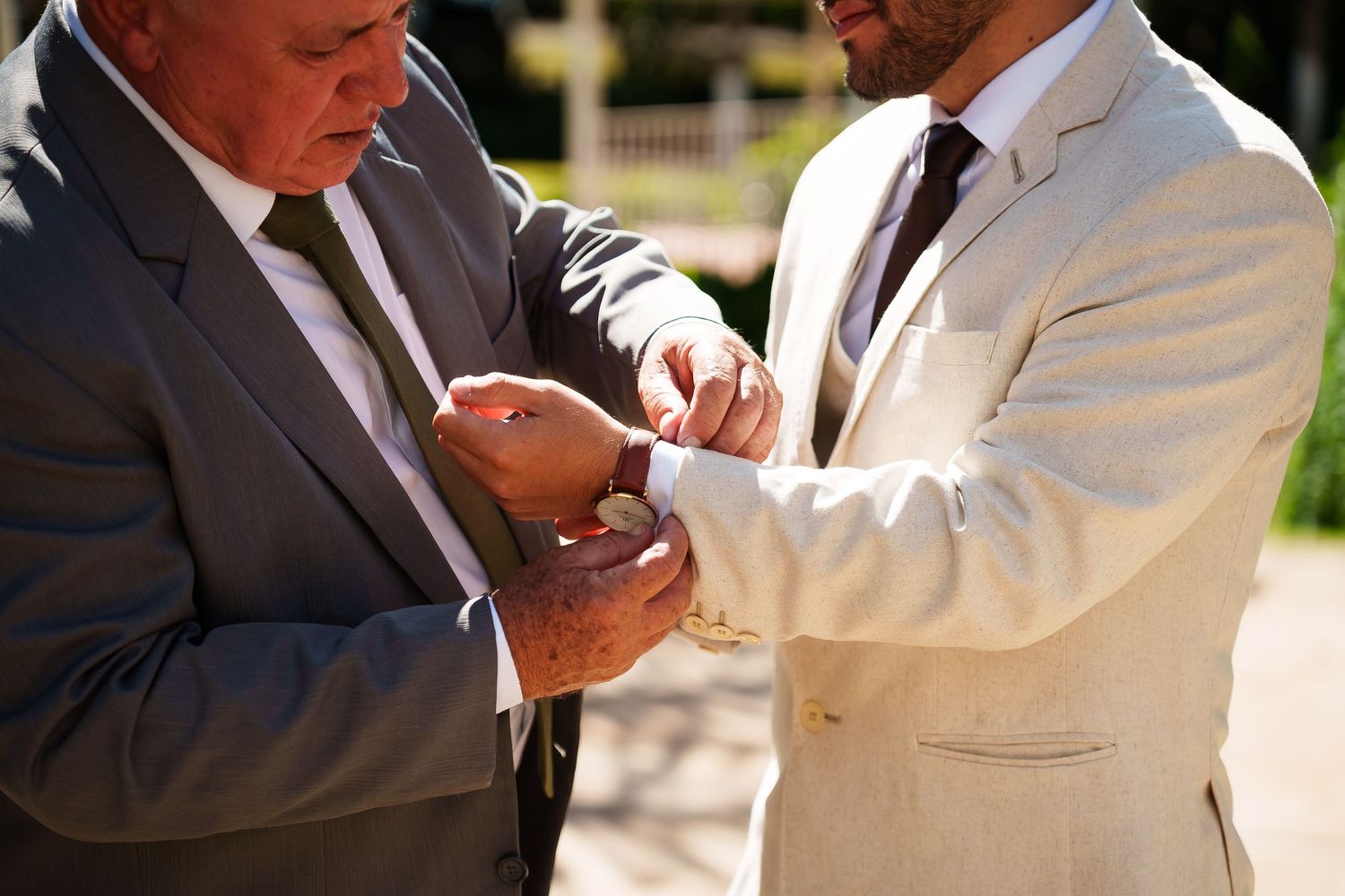 Two men in suits adjusting cufflinks outdoors at a formal event.