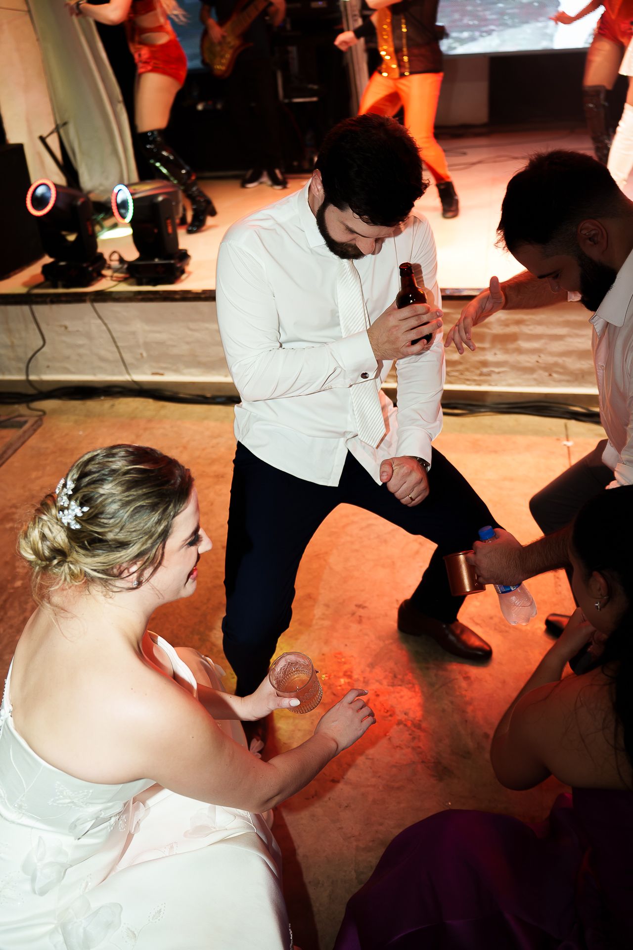 Bride in white gown and groom in white shirt dancing with guests at a wedding reception.