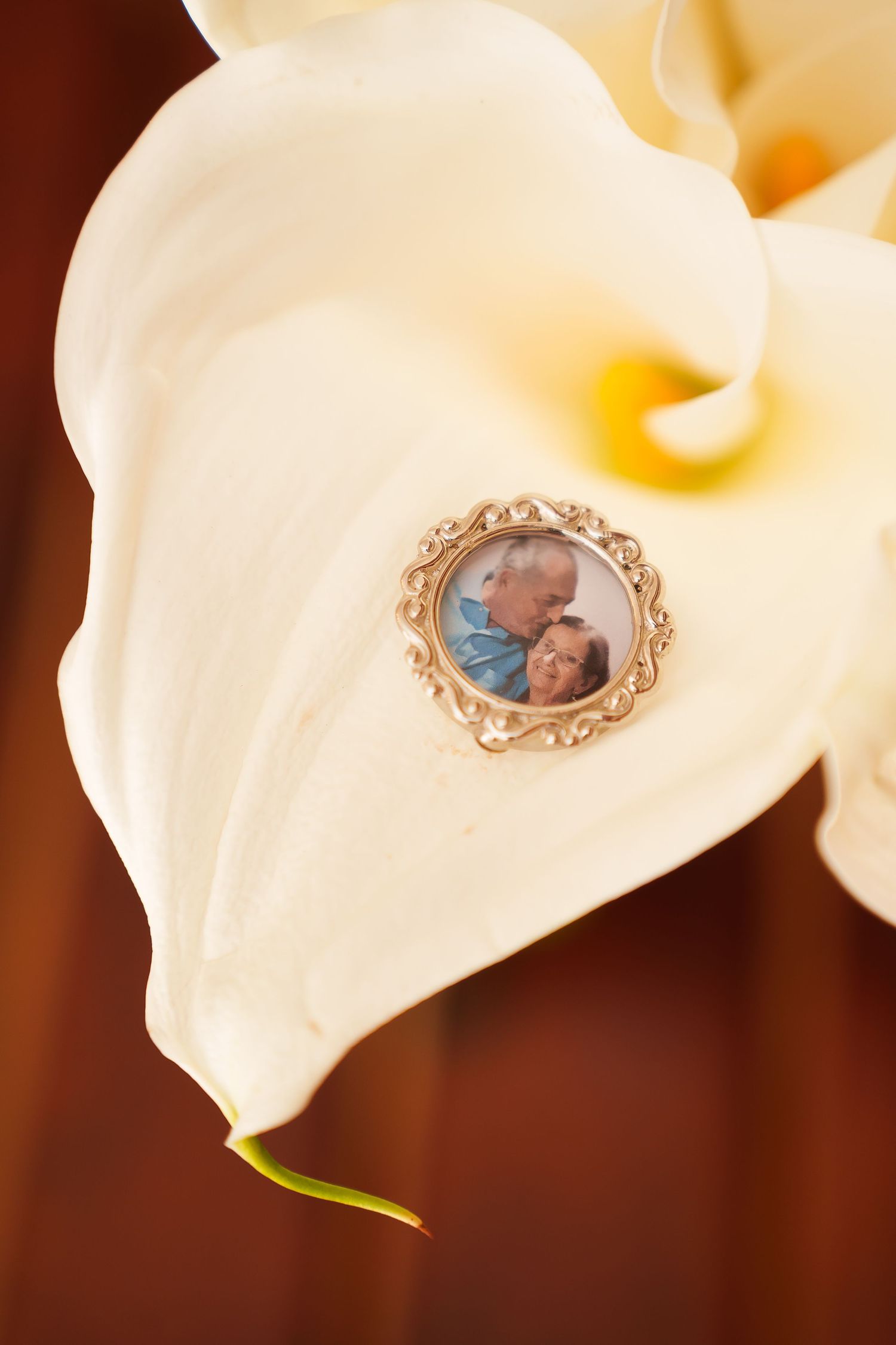 White calla lily with a small ornate gold photo locket brooch featuring a couple, placed on the petal.
