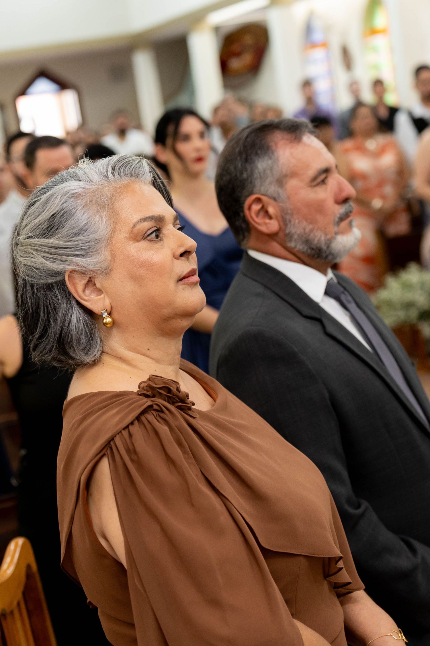 Elegant older couple attending a church wedding ceremony, woman in brown dress with gray hair, man in black suit.