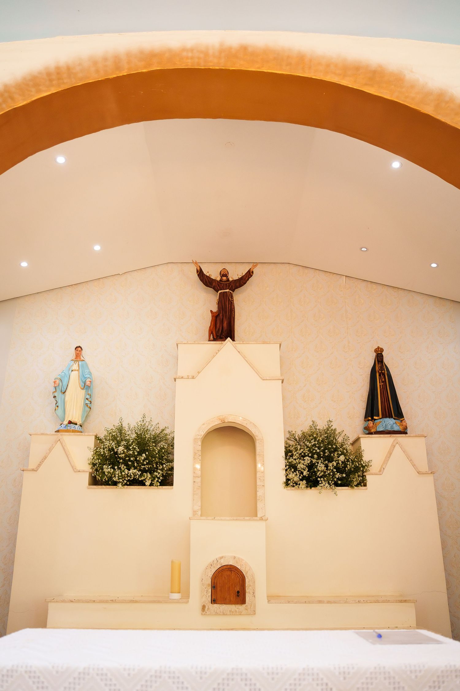 Catholic church altar with three religious statues including Jesus Christ with outstretched arms, flanked by Virgin Mary figures.