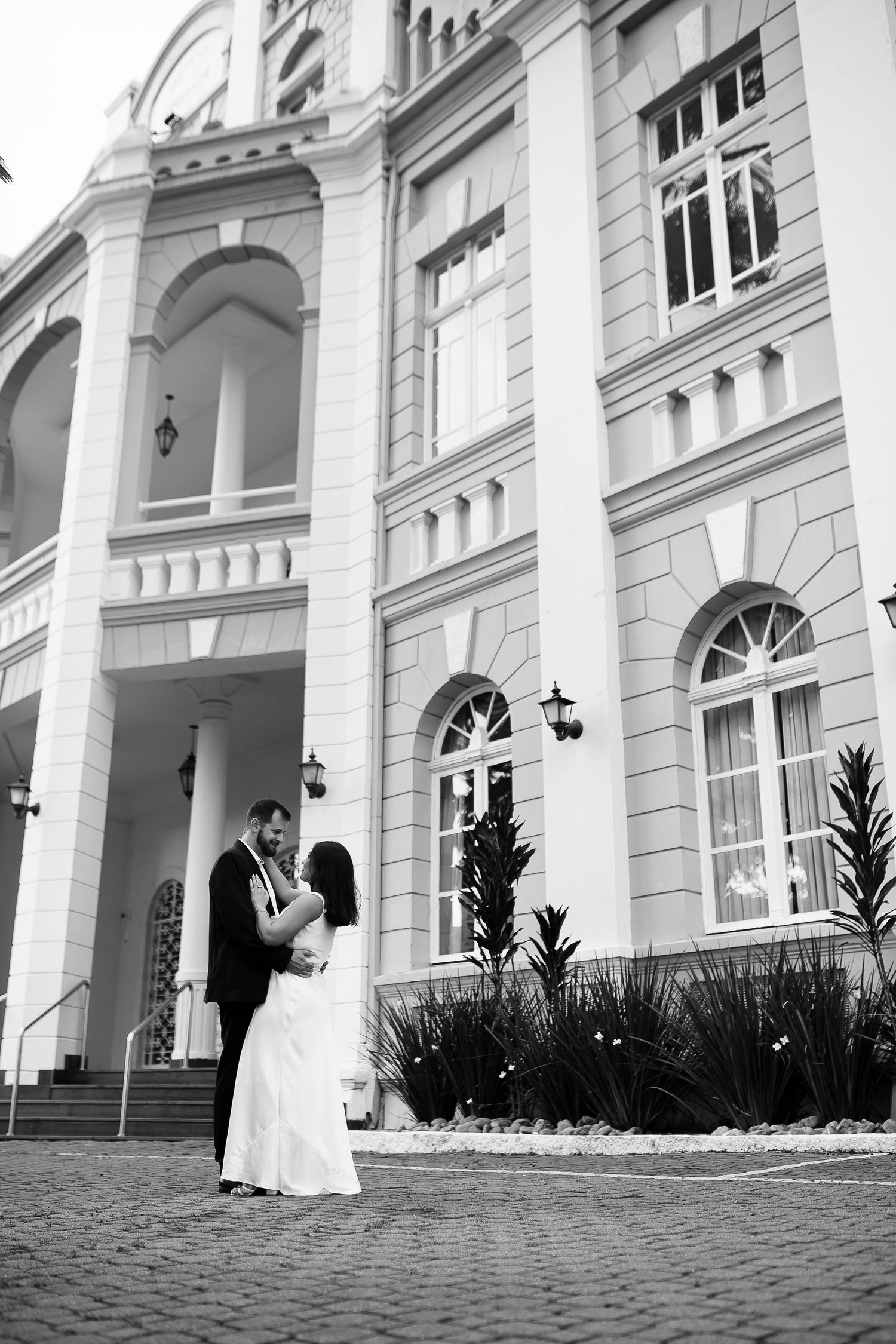 Black and white photo of a bride and groom embracing in front of a grand classical building.