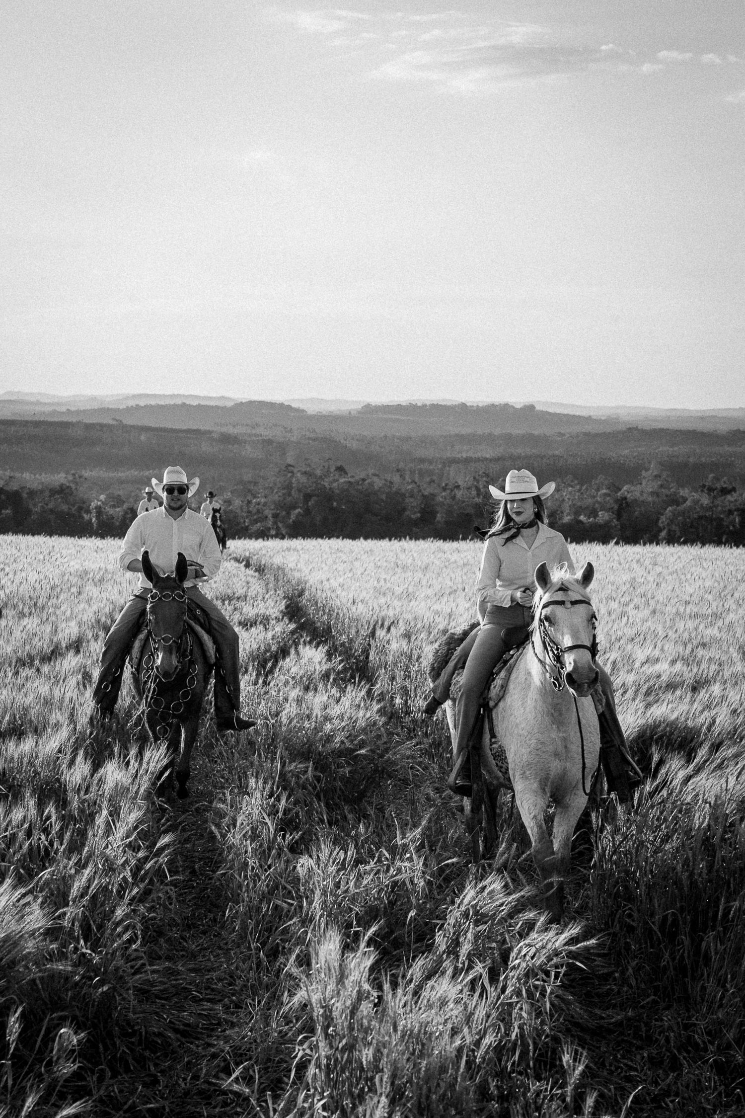 Two cowboys riding horses through a wheat field in black and white rural landscape photography.