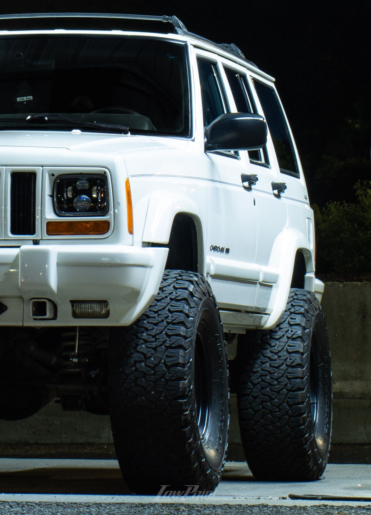 White Jeep Cherokee photographed at night inside a self-service car wash with moody lighting at night