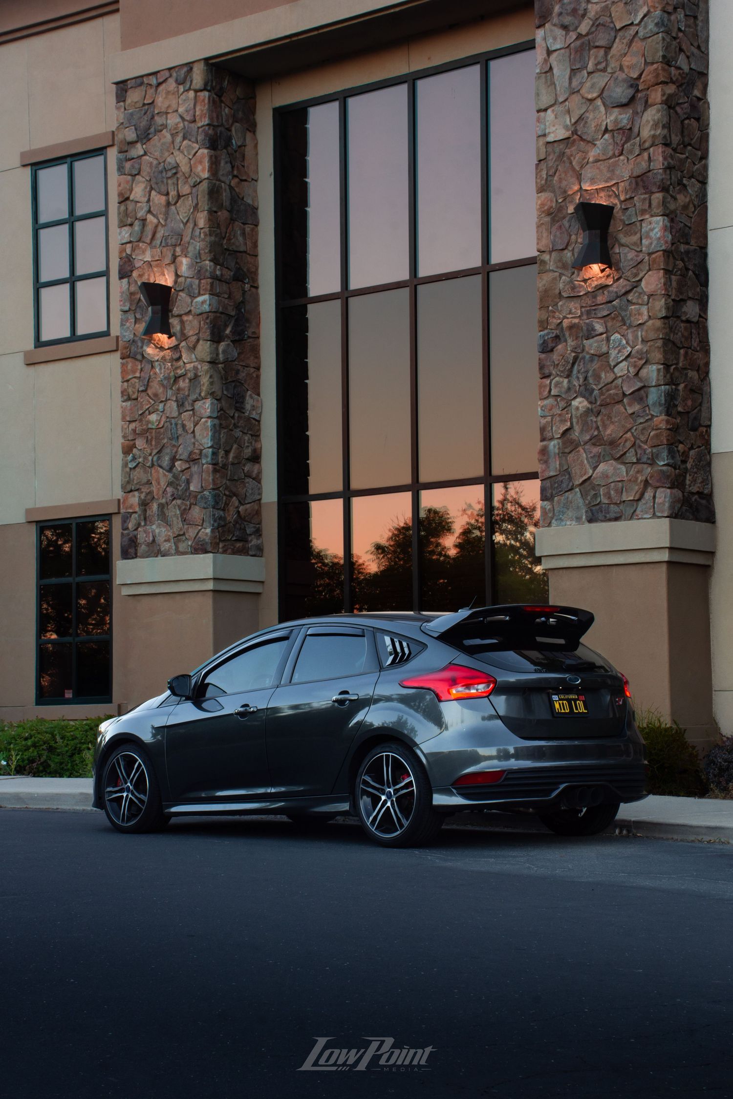 Magnetic Grey Ford Focus ST photographed in front of building with large modern windows reflecting a colorful sunset