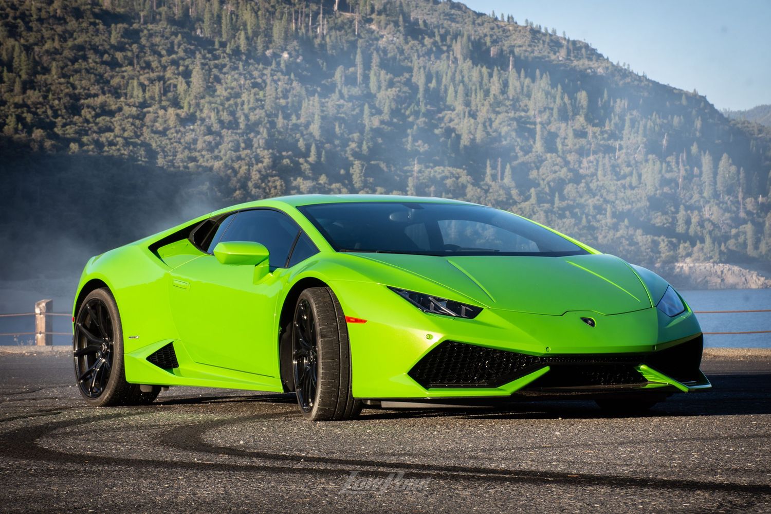 Green Lamborghini Huracan photographed in front of a lake with smoke from a burnout