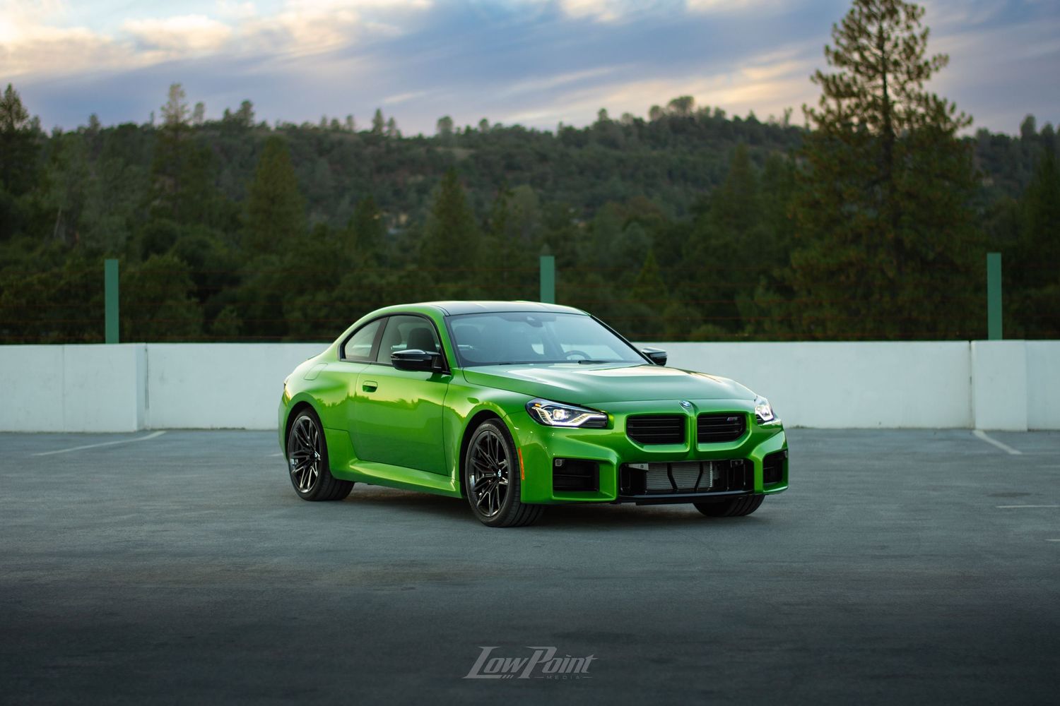 Java Green BMW photographed on the top of a parking garage during golden hour with moody clouds and trees in the background