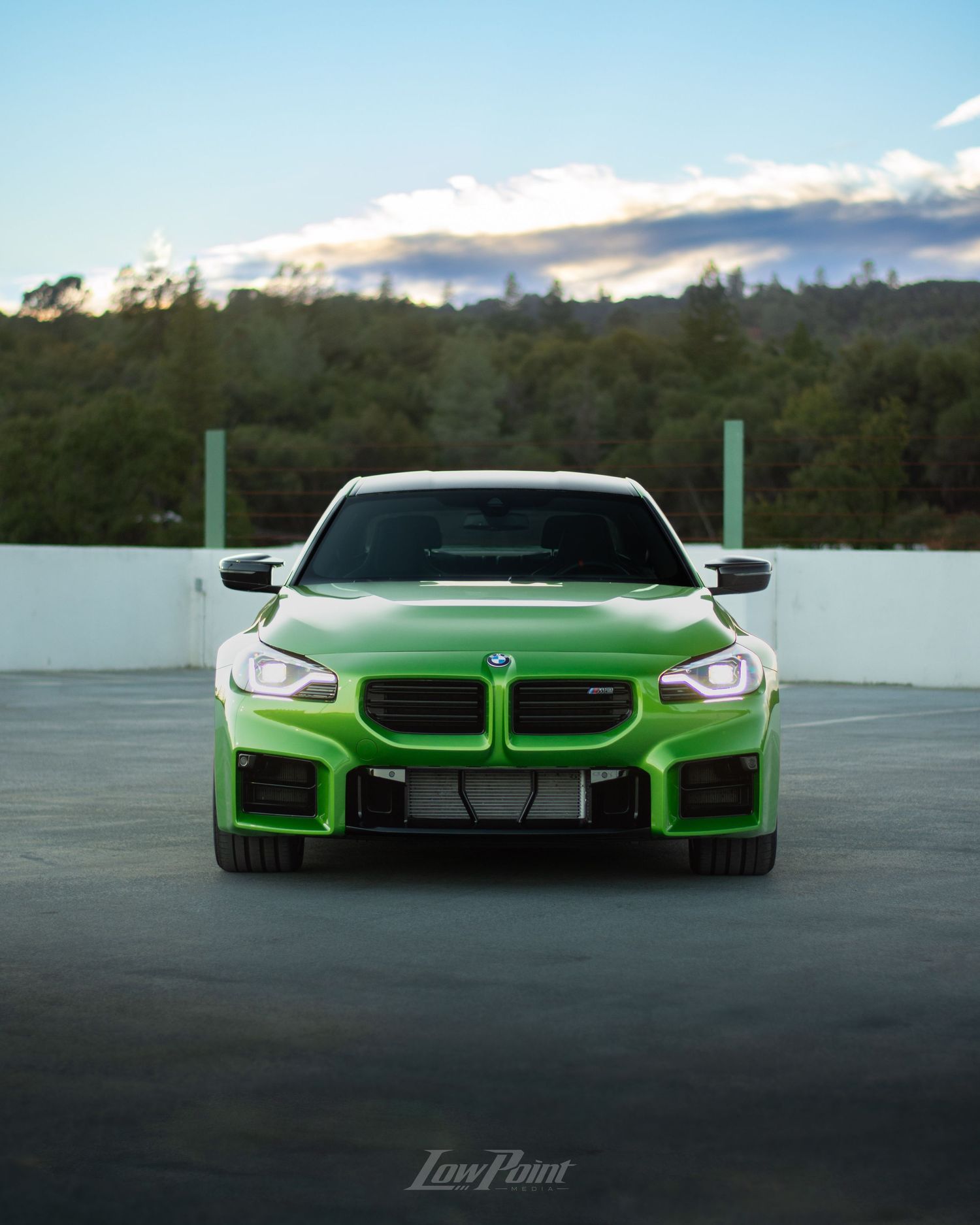 Java Green BMW photographed on the top of a parking garage during golden hour with moody clouds and trees in the background