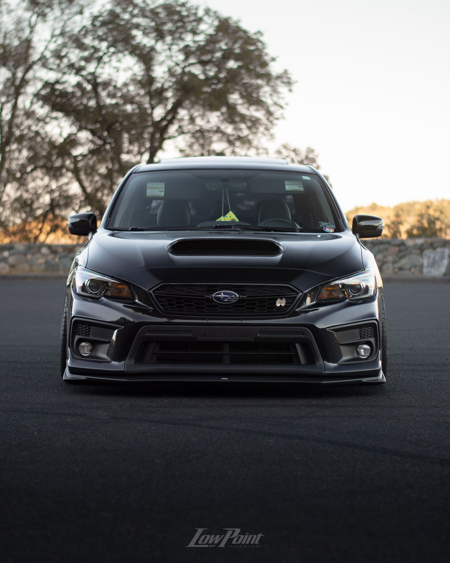 Black Subaru WRX photographed at a vista point overlooking a lake with a bridge