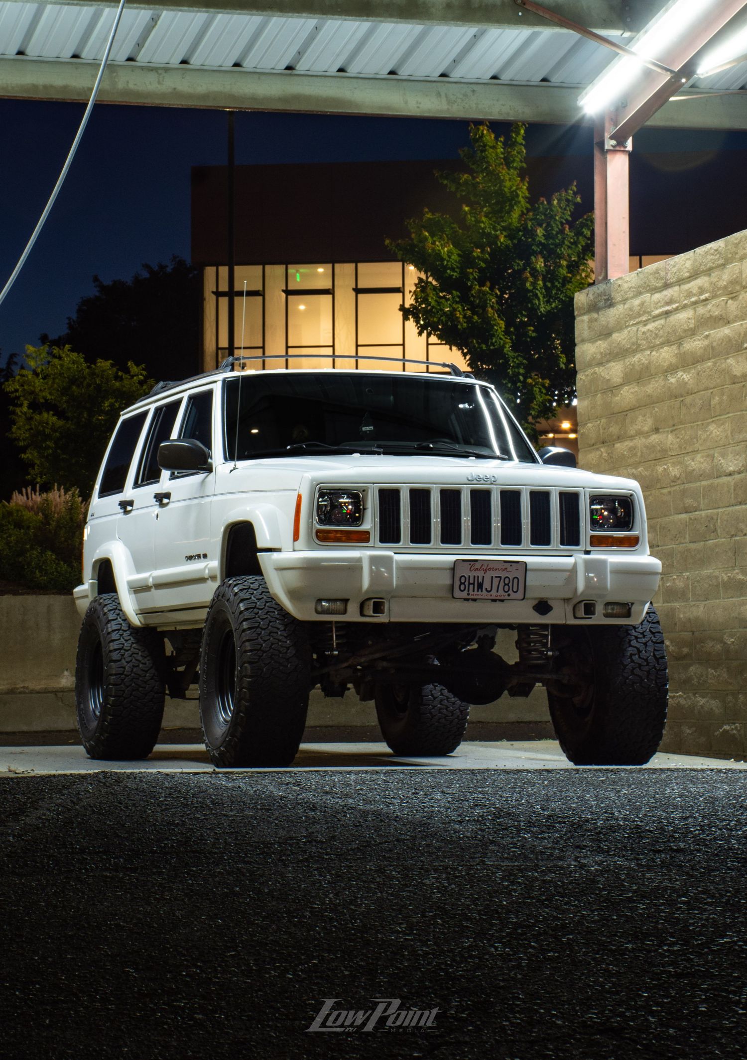 White Jeep Cherokee photographed at night inside a self-service car wash with moody lighting at night