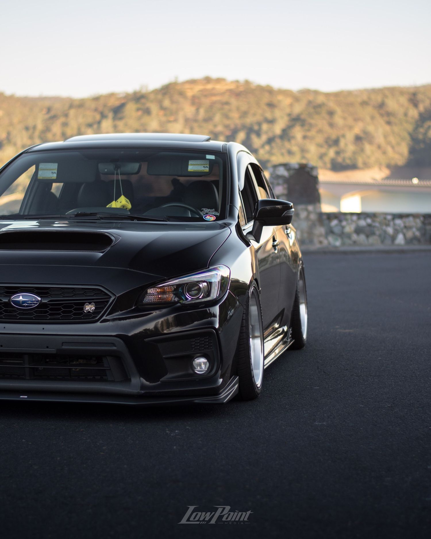 Black Subaru WRX photographed at a vista point overlooking a lake with a bridge