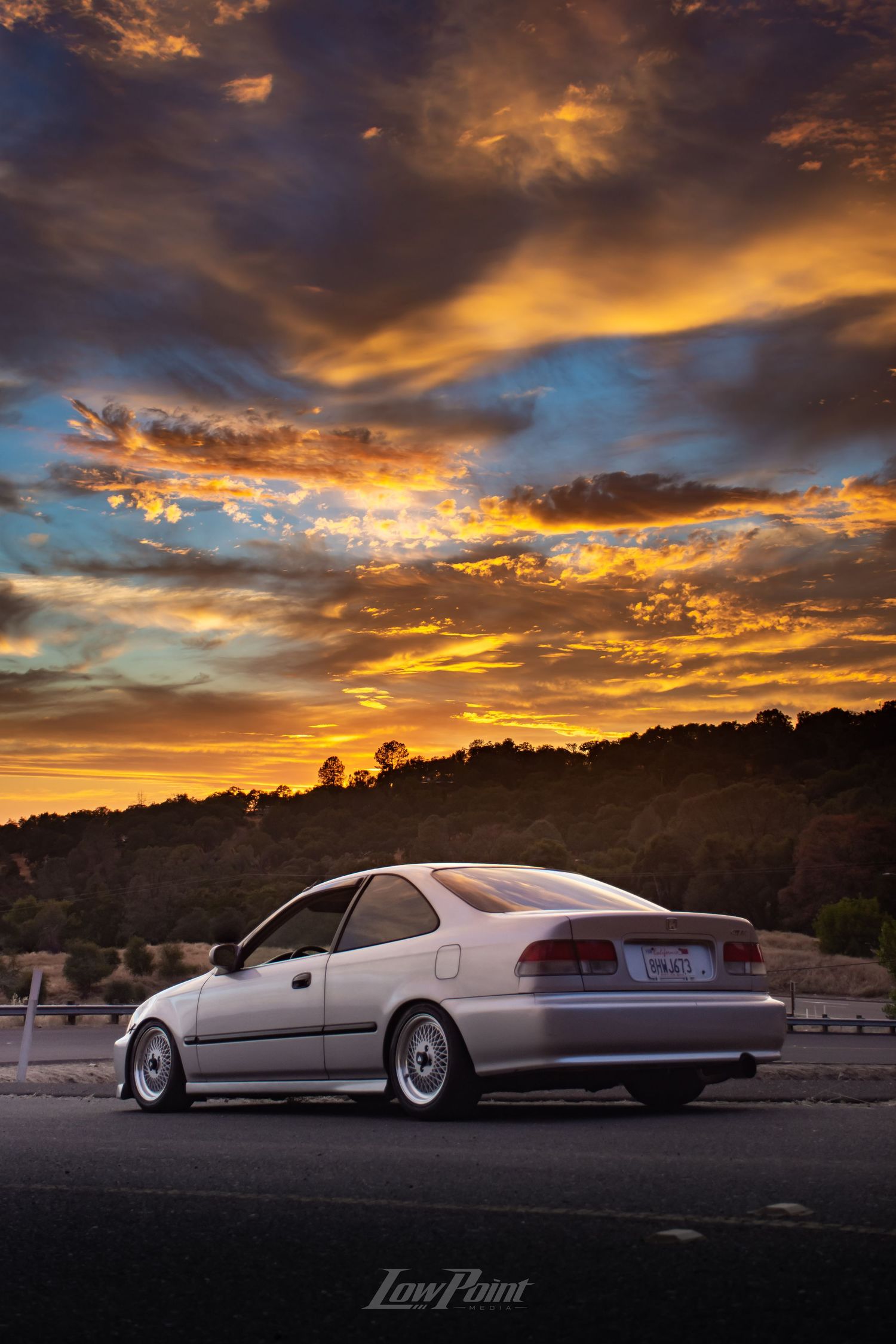 Silver Honda Civic photographed in front of painted sunset sky
