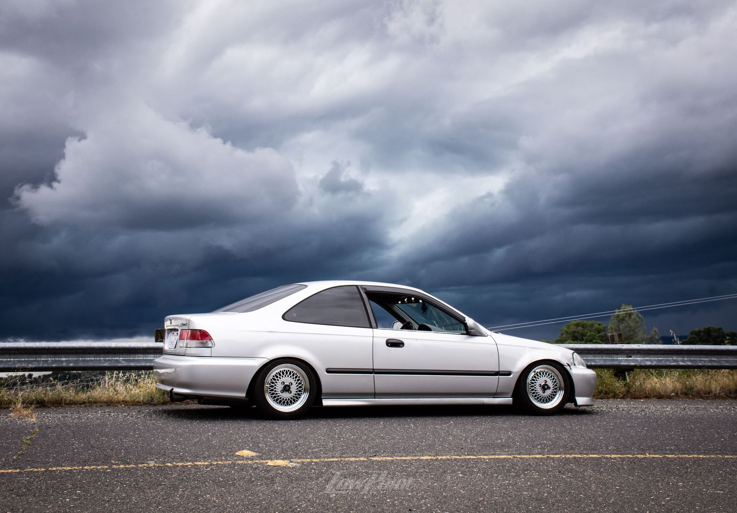 Silver Honda Civic photographed with blue and grey rain clouds in background