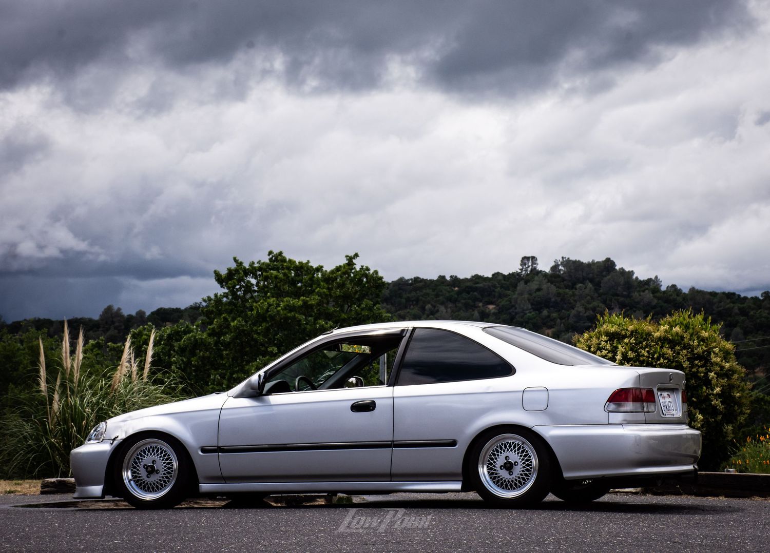Silver Honda Civic photographed with blue and grey rain clouds in background