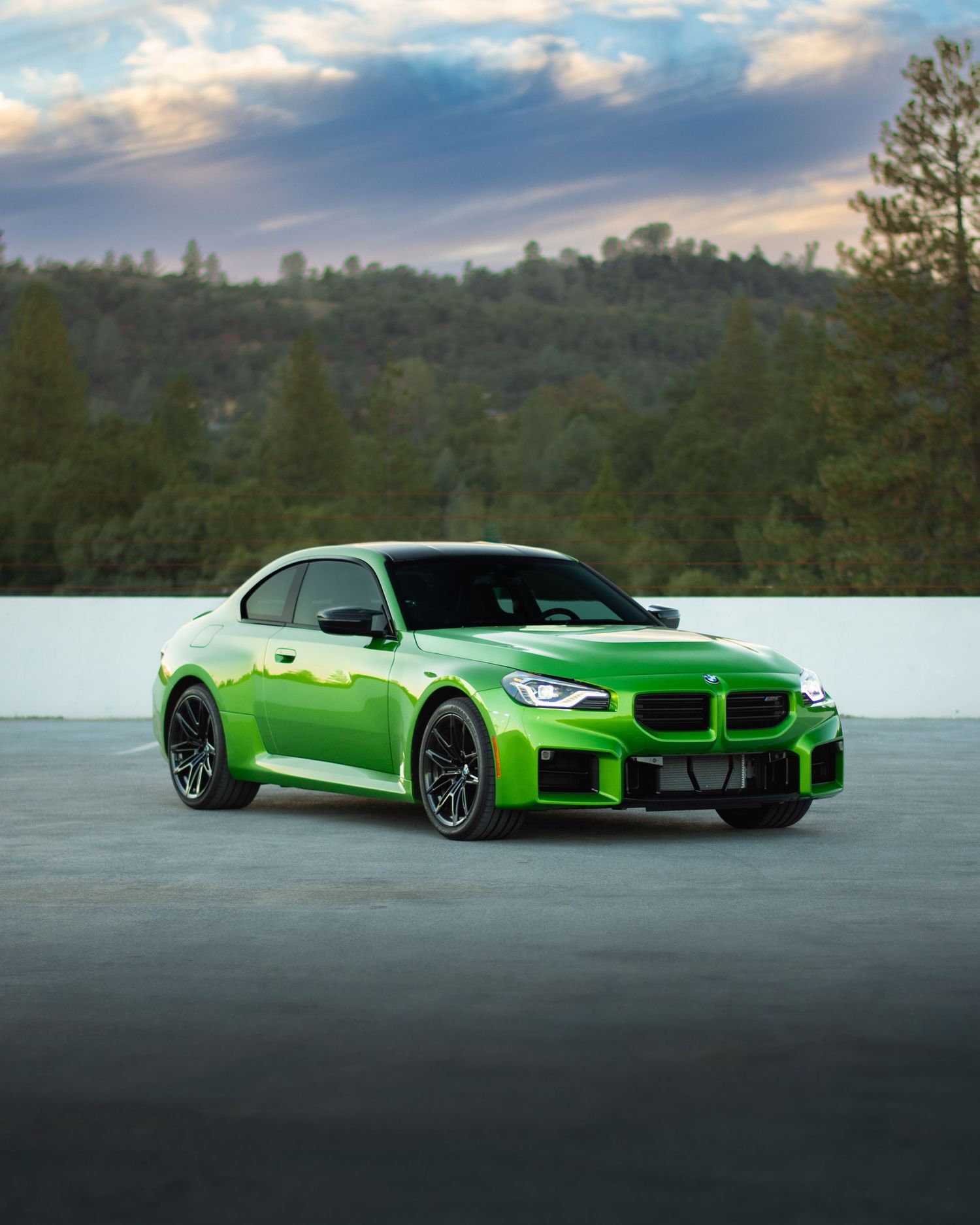 Java Green BMW photographed on the top of a parking garage during golden hour with moody clouds and trees in the background
