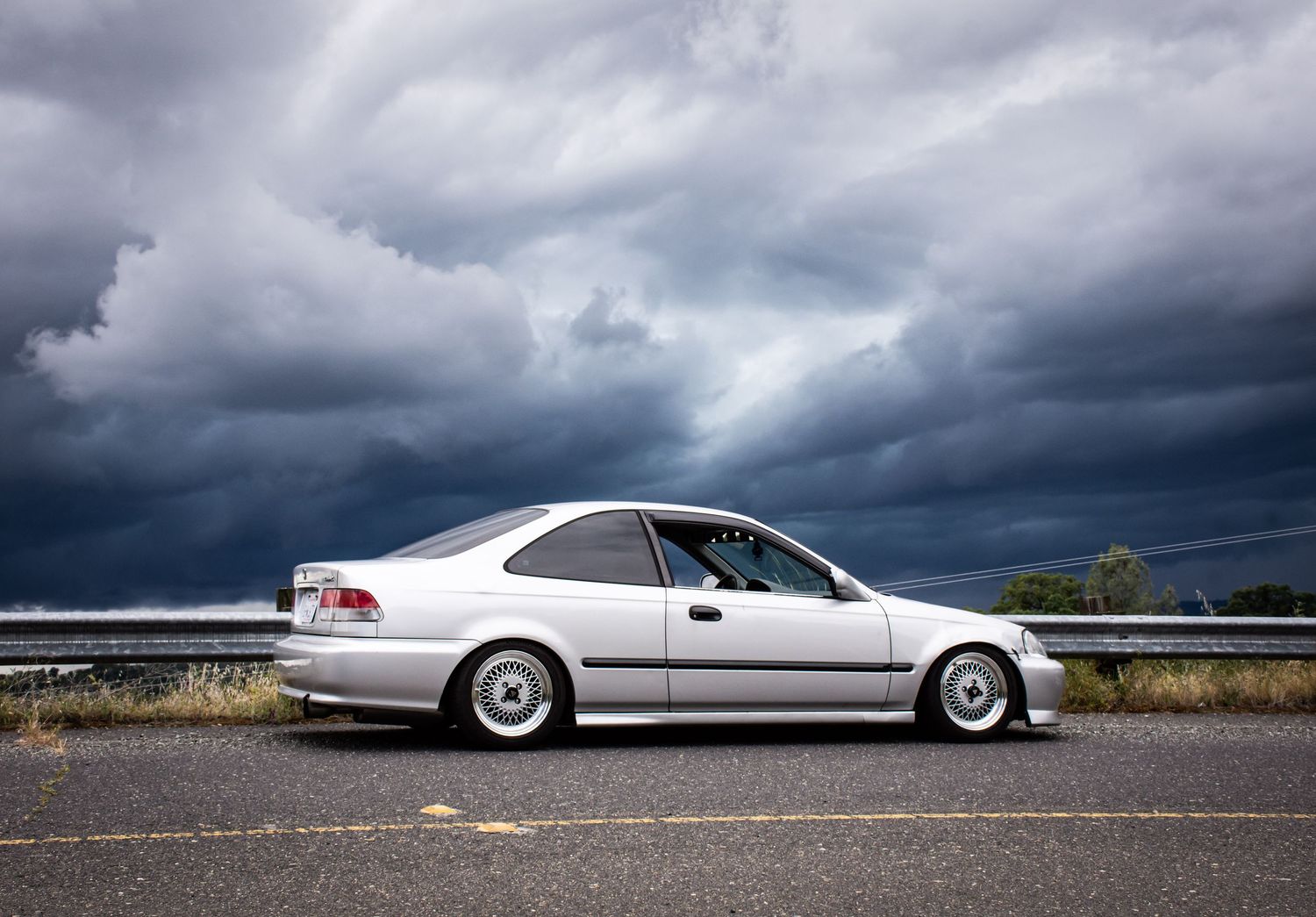 Silver Honda Civic photographed with blue and grey rain clouds in background