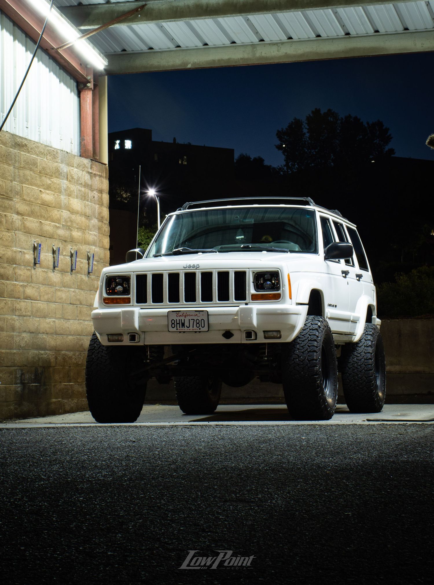 White Jeep Cherokee photographed at night inside a self-service car wash with moody lighting at night
