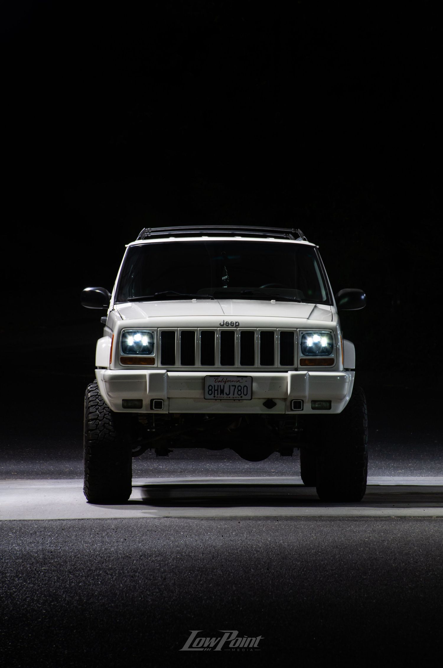 White Jeep Cherokee photographed at night inside a self-service car wash with moody lighting at night