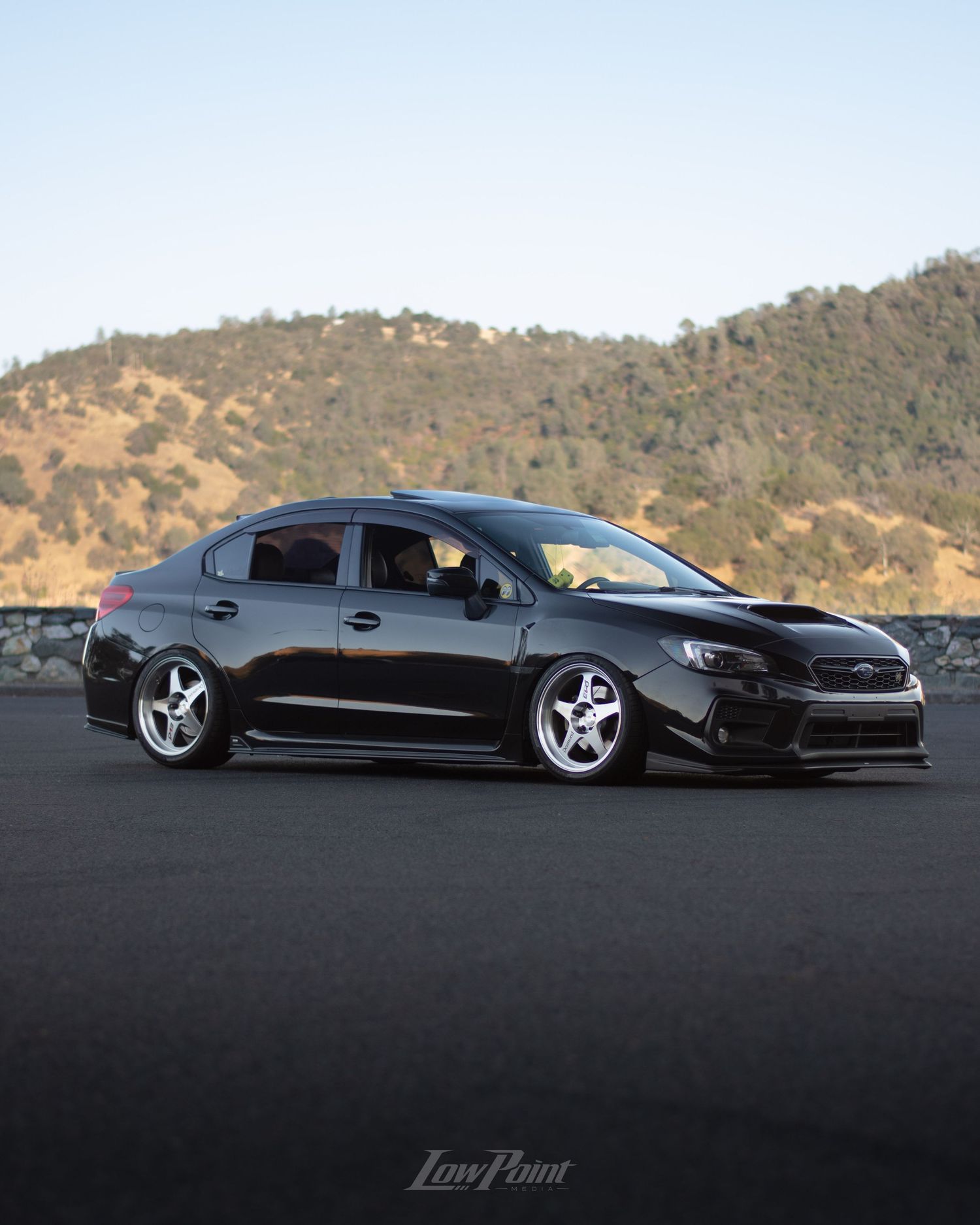 Black Subaru WRX photographed at a vista point overlooking a lake with a bridge