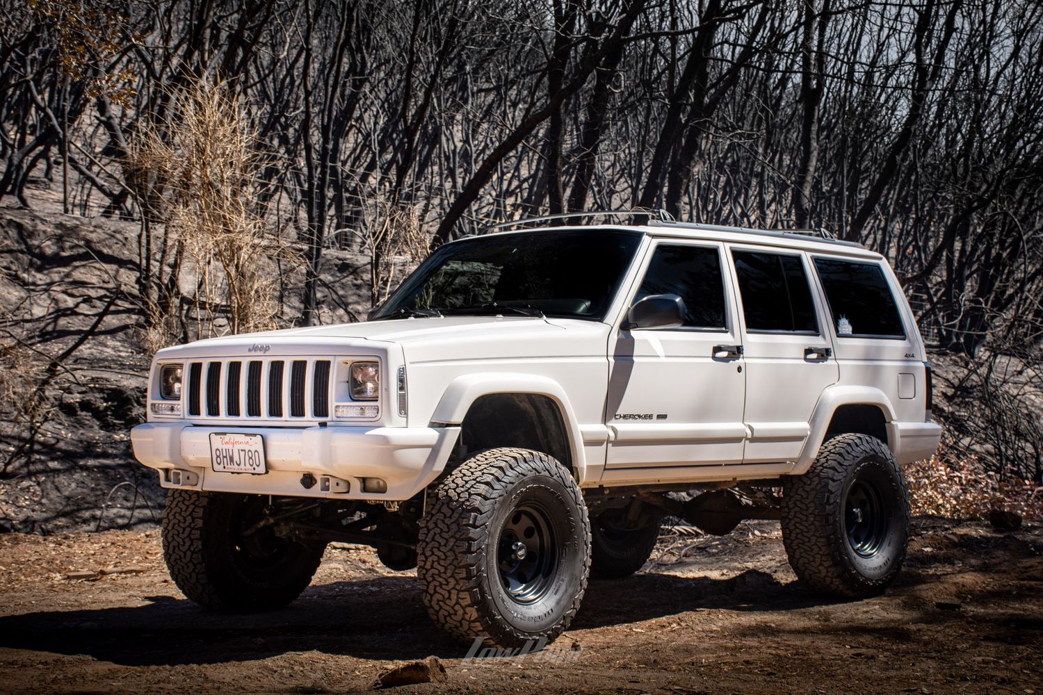 White Jeep Cherokee photographed in front of black burned trees from a forest fire