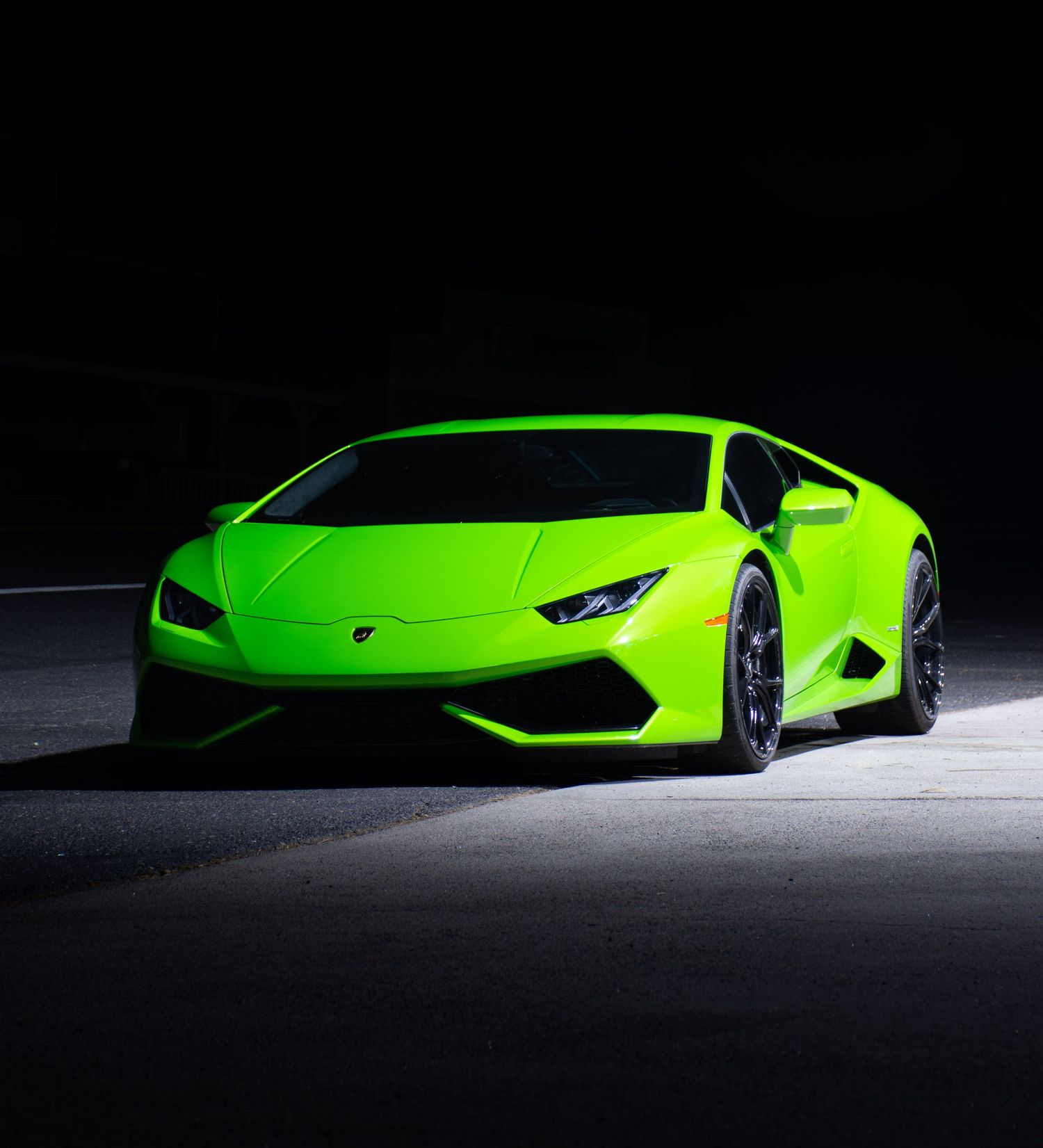 Green Lamborghini Huracan photographed with moody lighting and black background at night