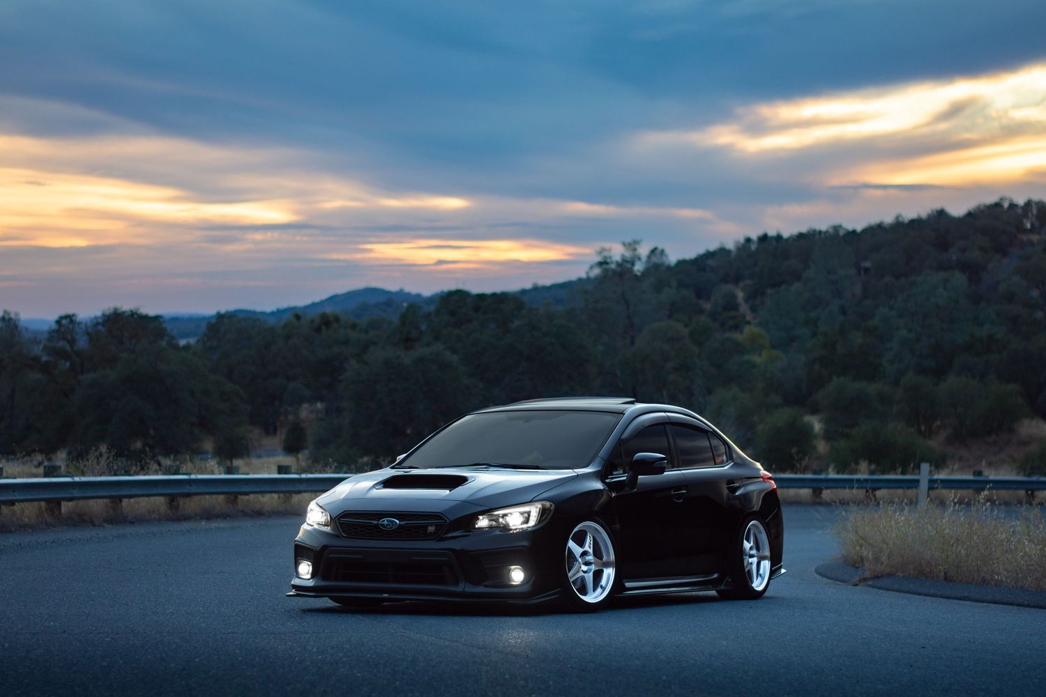 Black Subaru WRX photographed in front of a moody sunset with blue and orange clouds