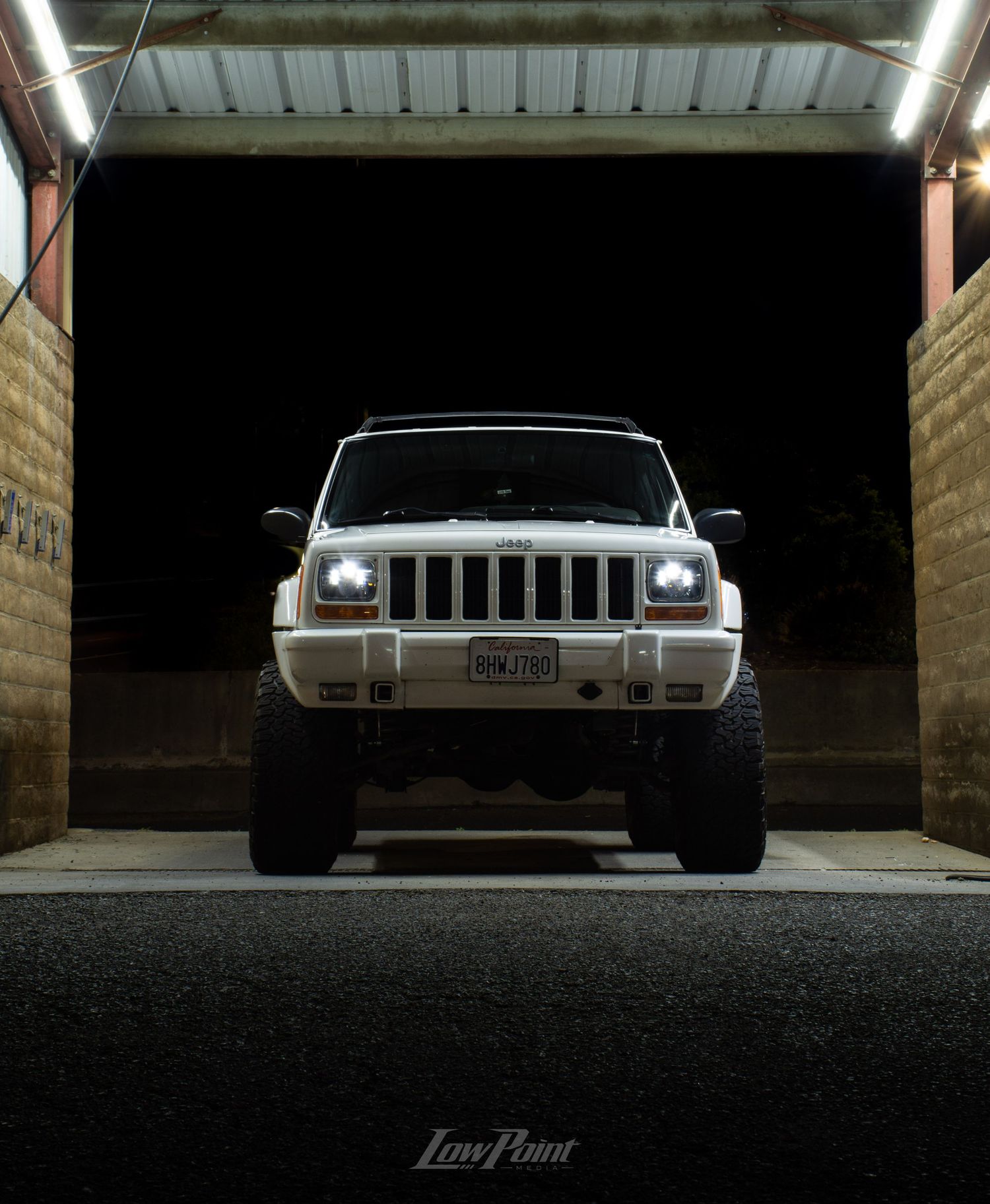 White Jeep Cherokee photographed at night inside a self-service car wash with moody lighting at night