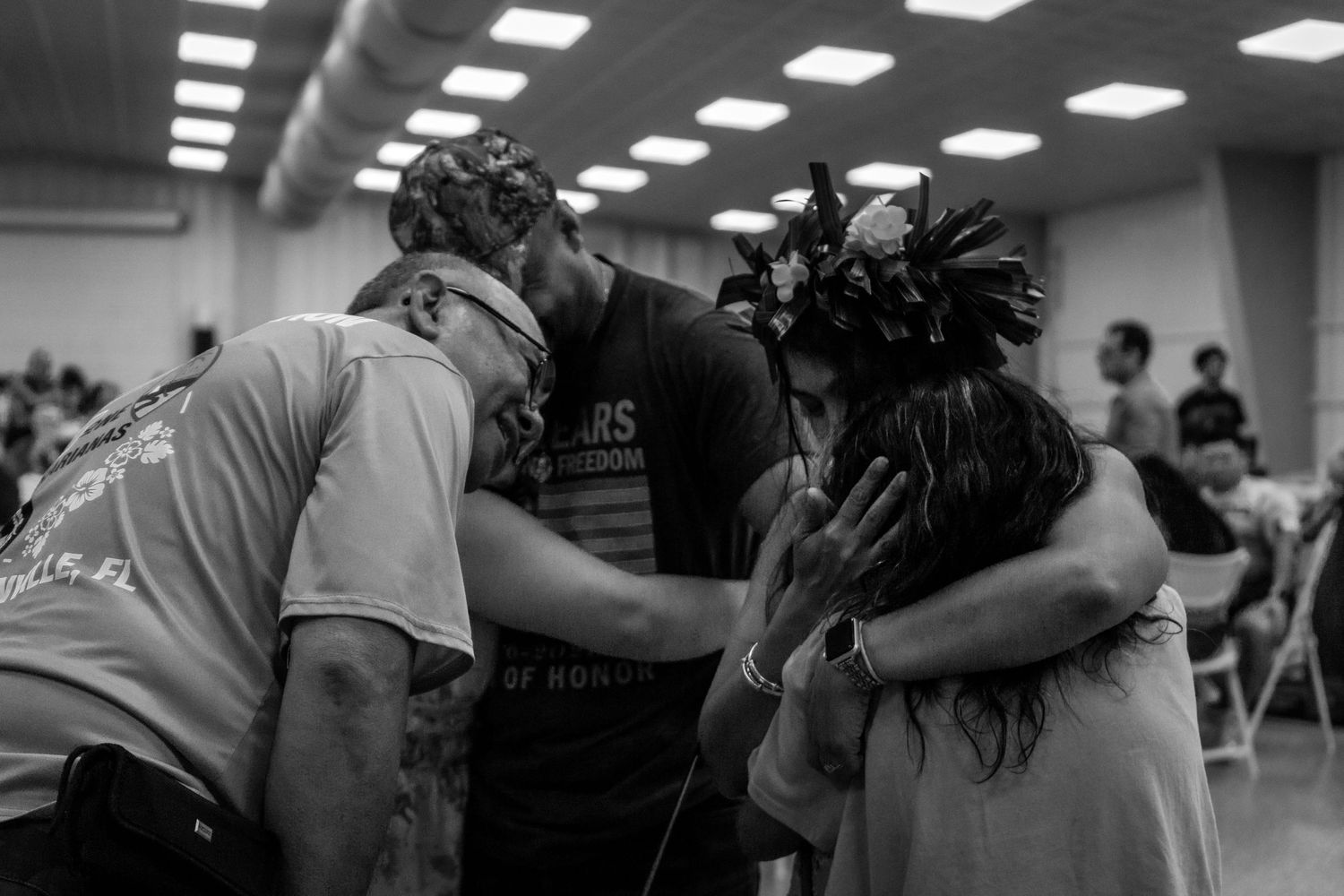 Emotional black and white photo of three people sharing a heartfelt embrace at cultural gathering.