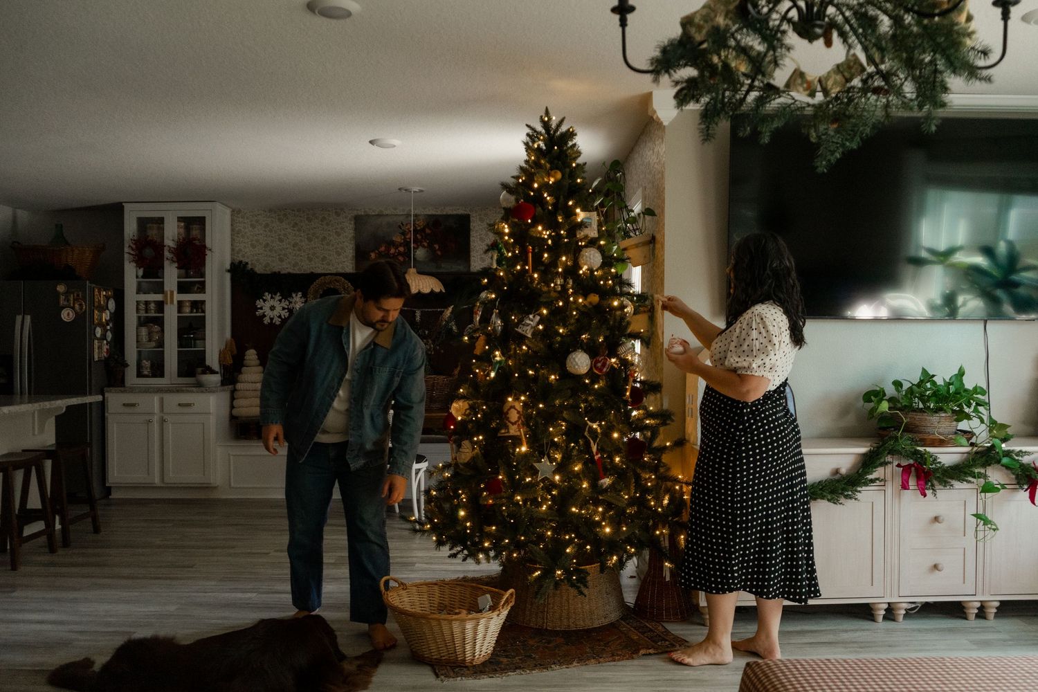 Couple decorating a Christmas tree with lights and ornaments in a cozy home living room during the holiday season.