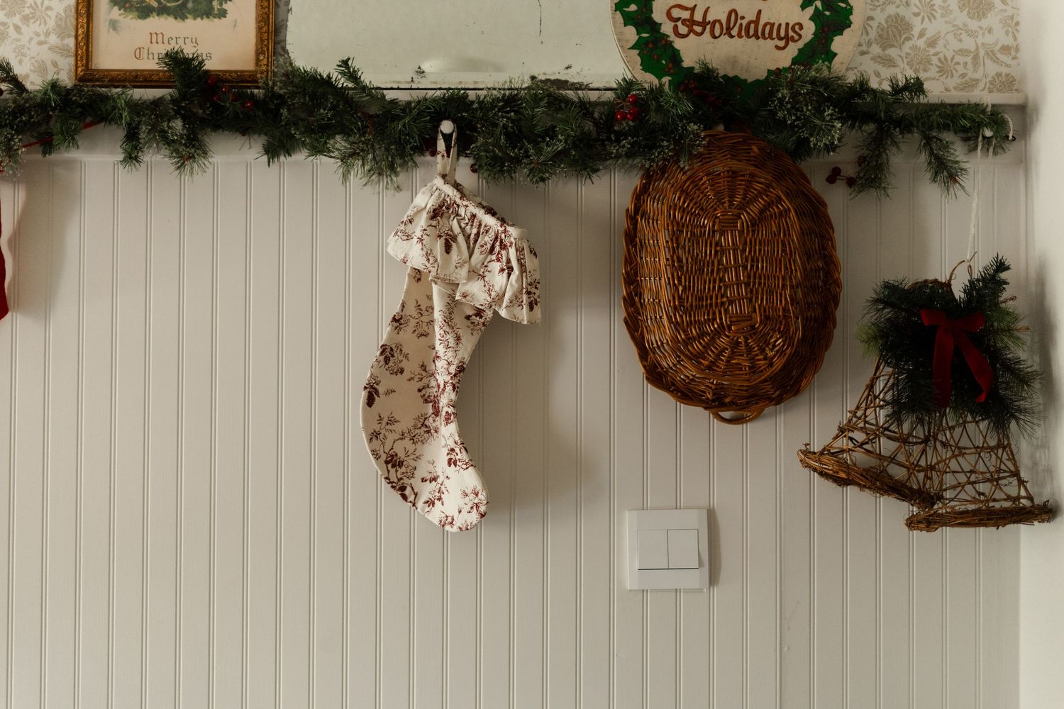 Christmas mantel decorated with garland, a floral stocking, wicker basket, and golden bell ornaments.