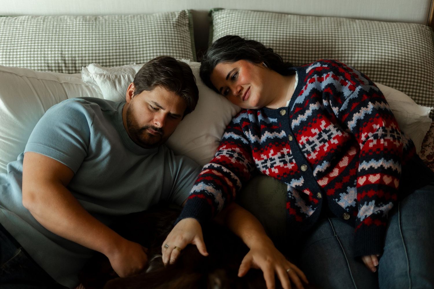 Couple relaxing together on a couch, man in gray shirt and woman in colorful sweater sharing a tender moment.
