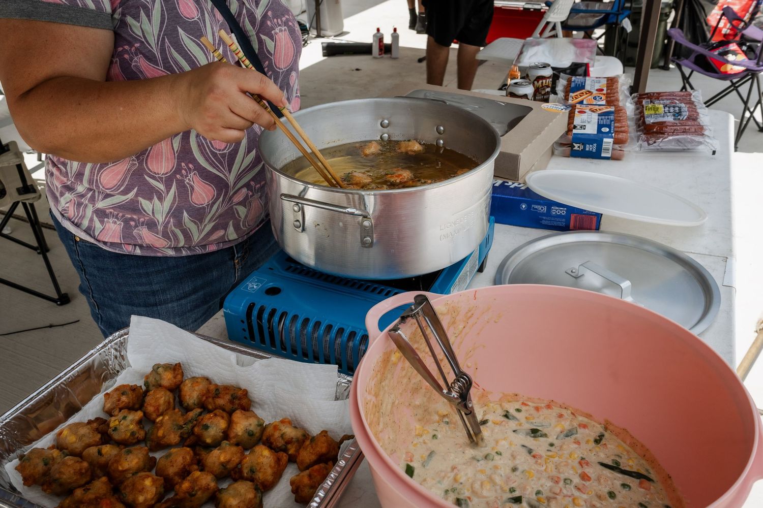 Person stirring a large pot of soup at an outdoor food booth with fried food and dip nearby.