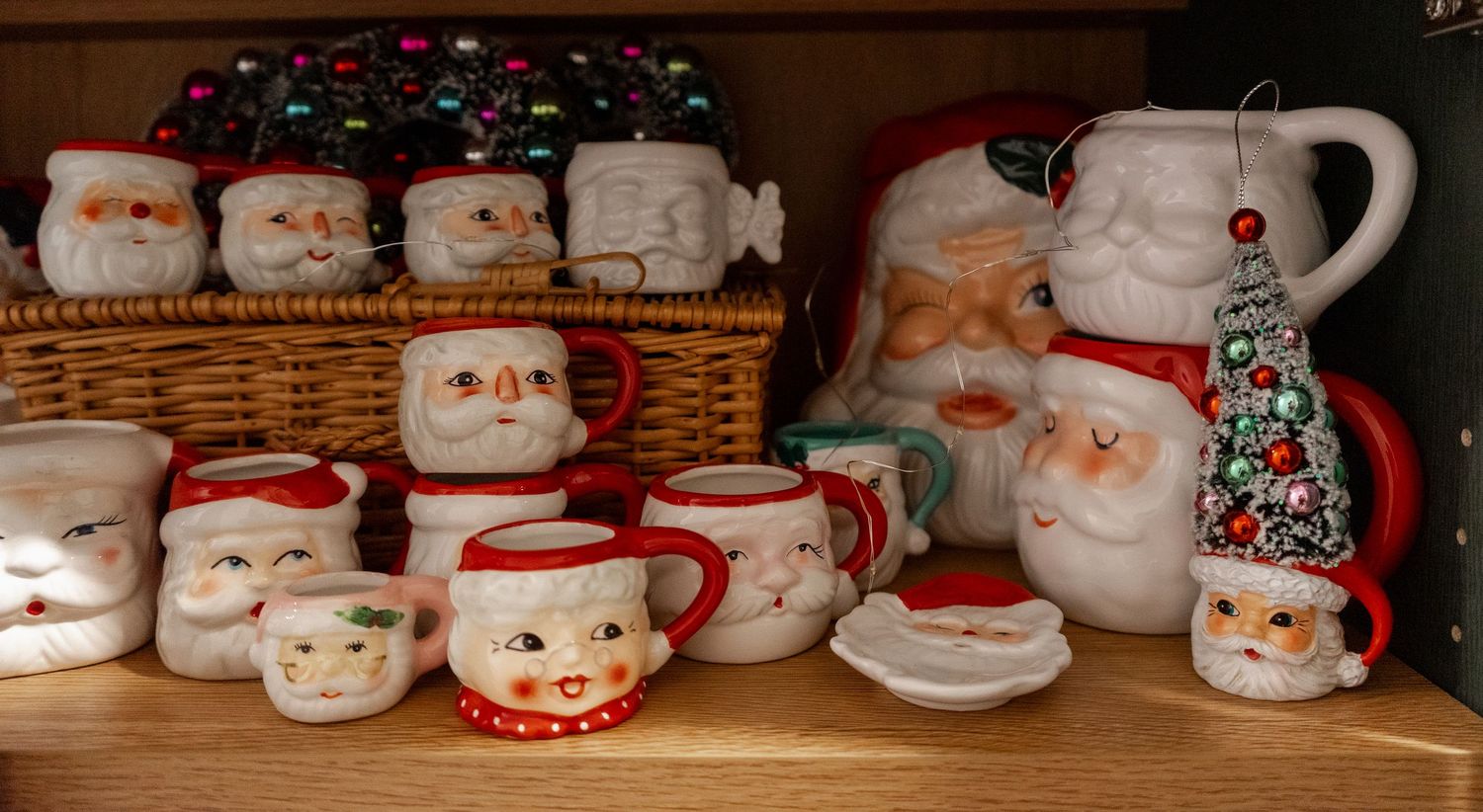 Collection of vintage Santa Claus ceramic mugs and pitchers displayed on wooden shelves with a wicker basket.