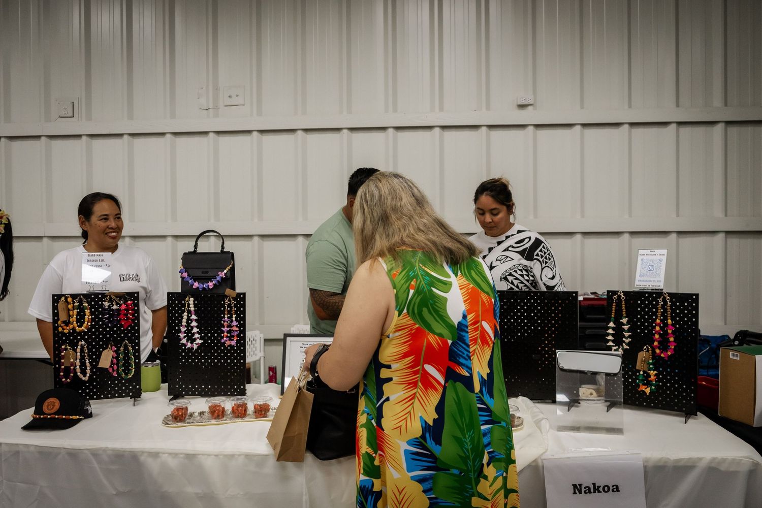 Vendors and shoppers browse jewelry and accessories at a cultural marketplace booth.