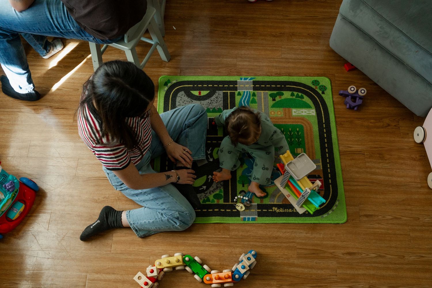 Overhead view of mother and child playing on a road map play mat with toys on hardwood floor.
