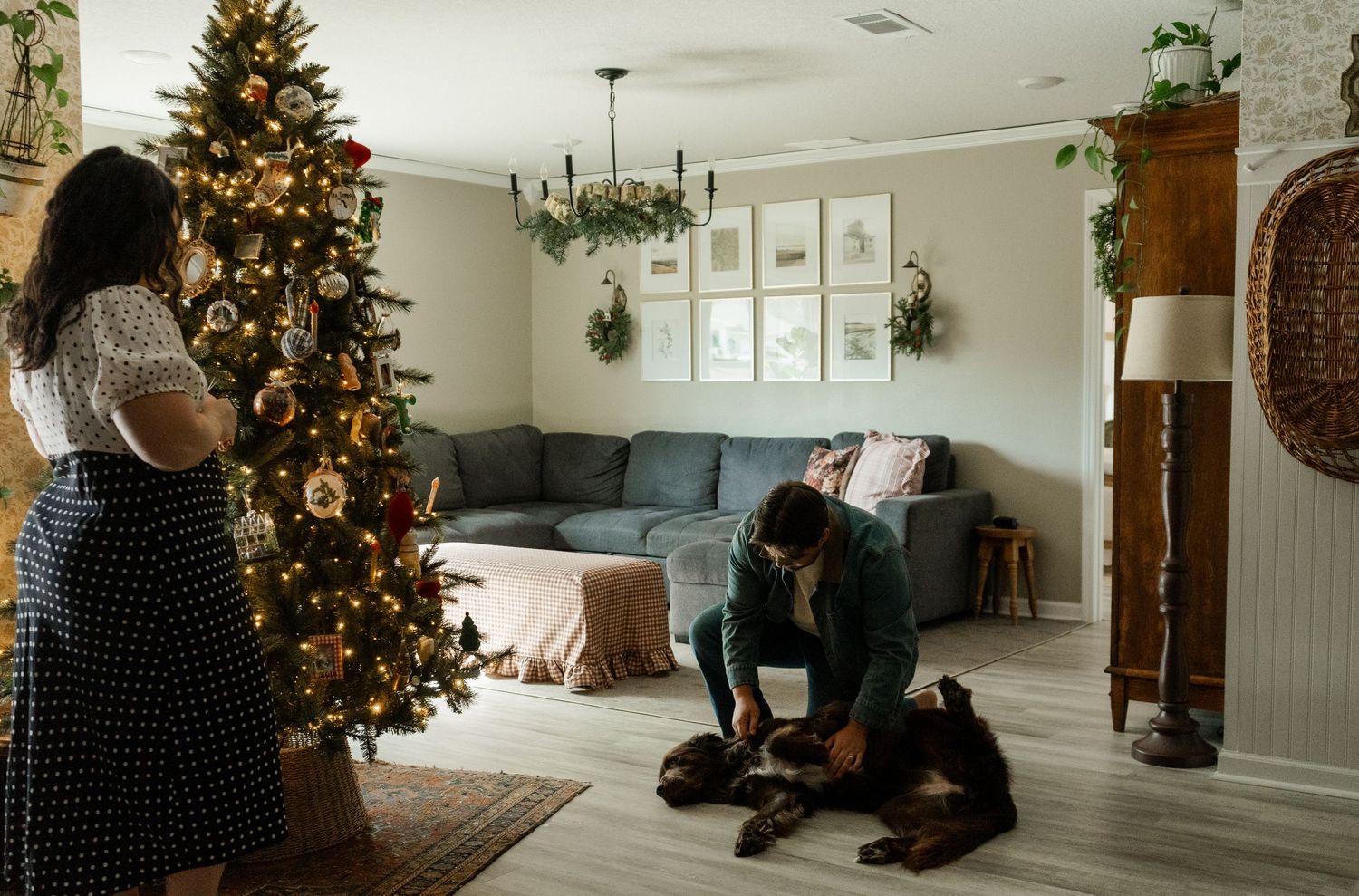 Family decorating Christmas tree in cozy living room with dog, holiday wreath, and festive lights.