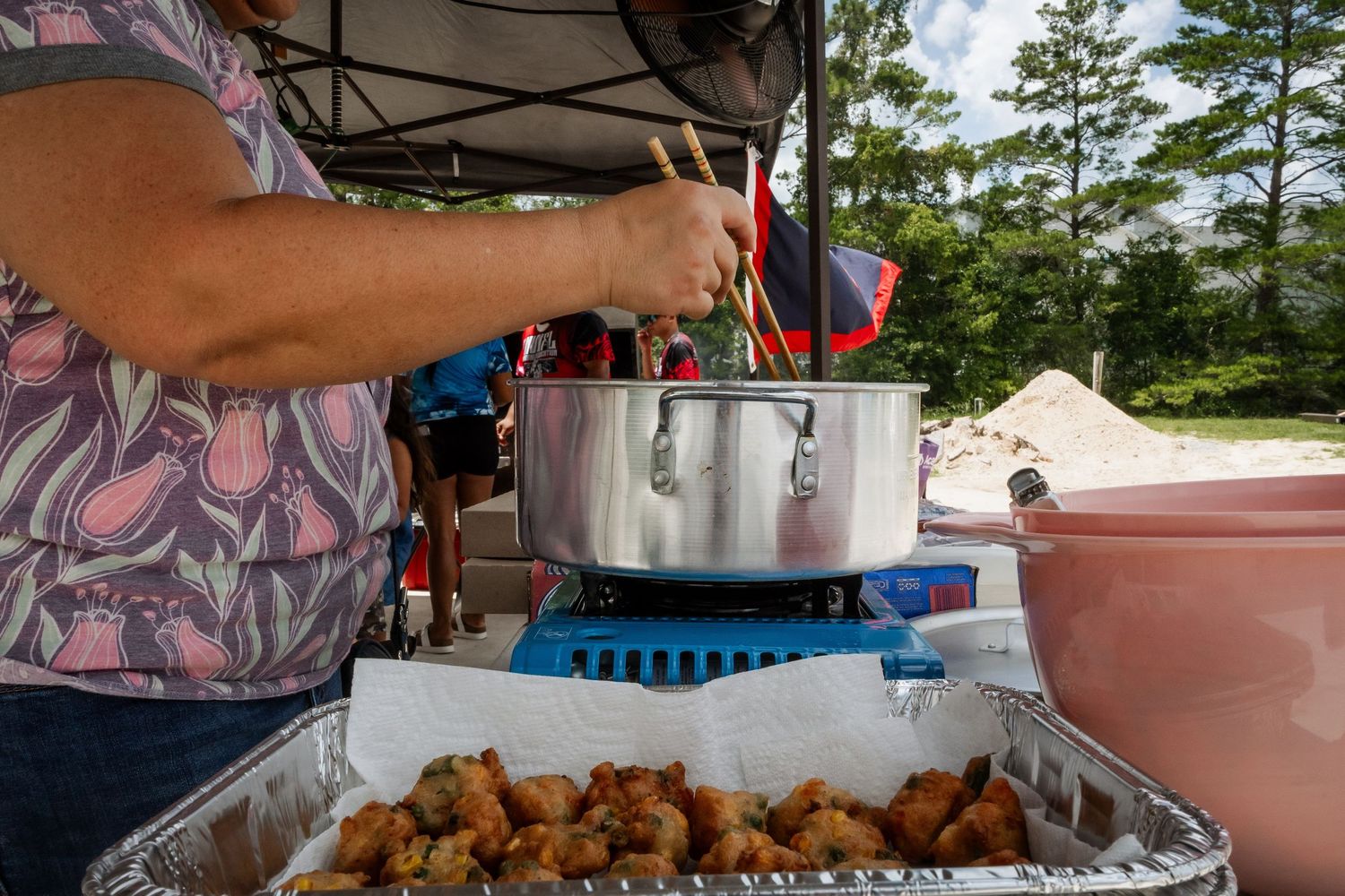 A woman stirs a large pot while cooking traditional fried food at an outdoor event.