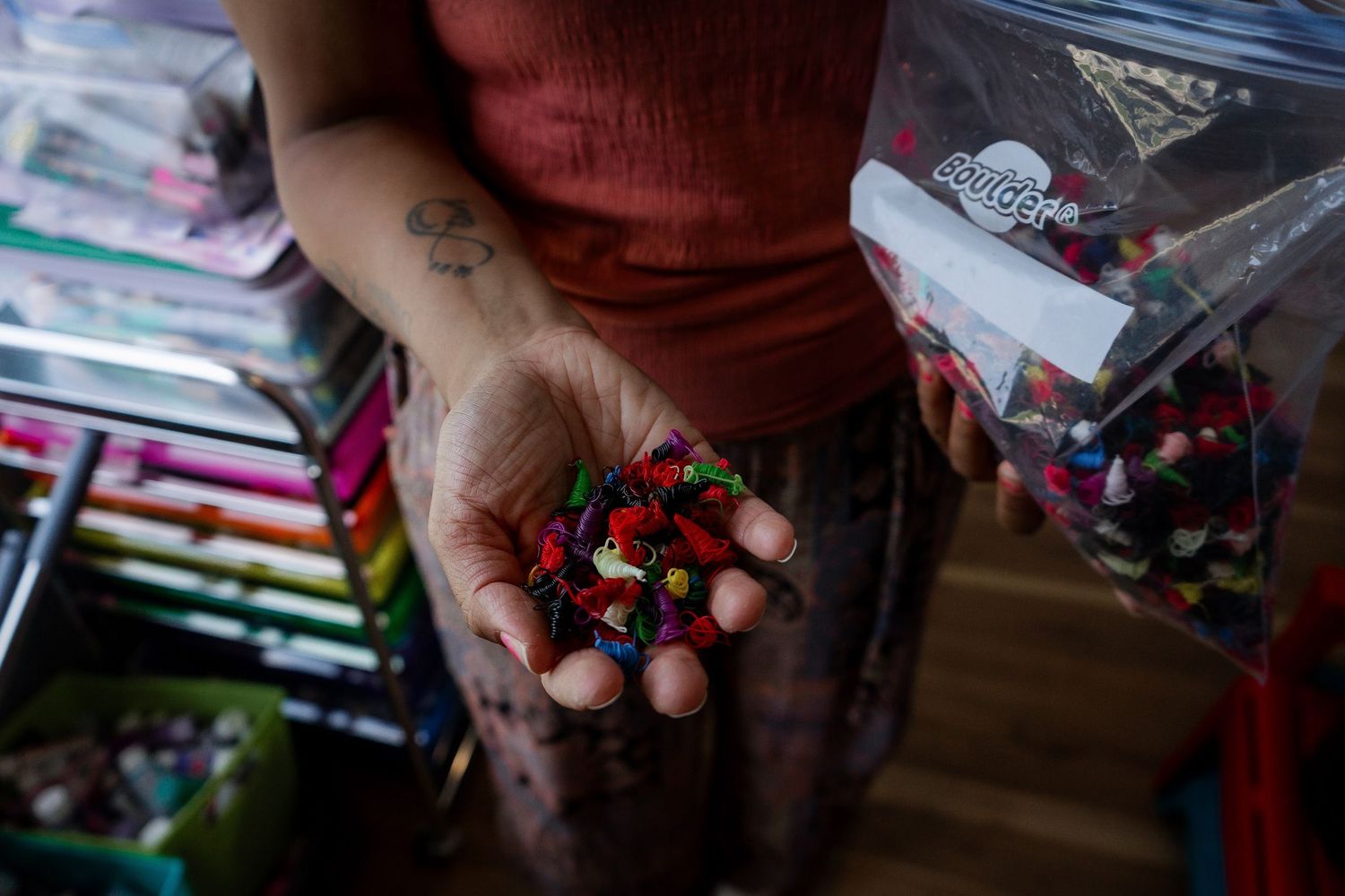 Close-up of woman's hand holding small colorful hair accessories near packaged craft supplies in a store.