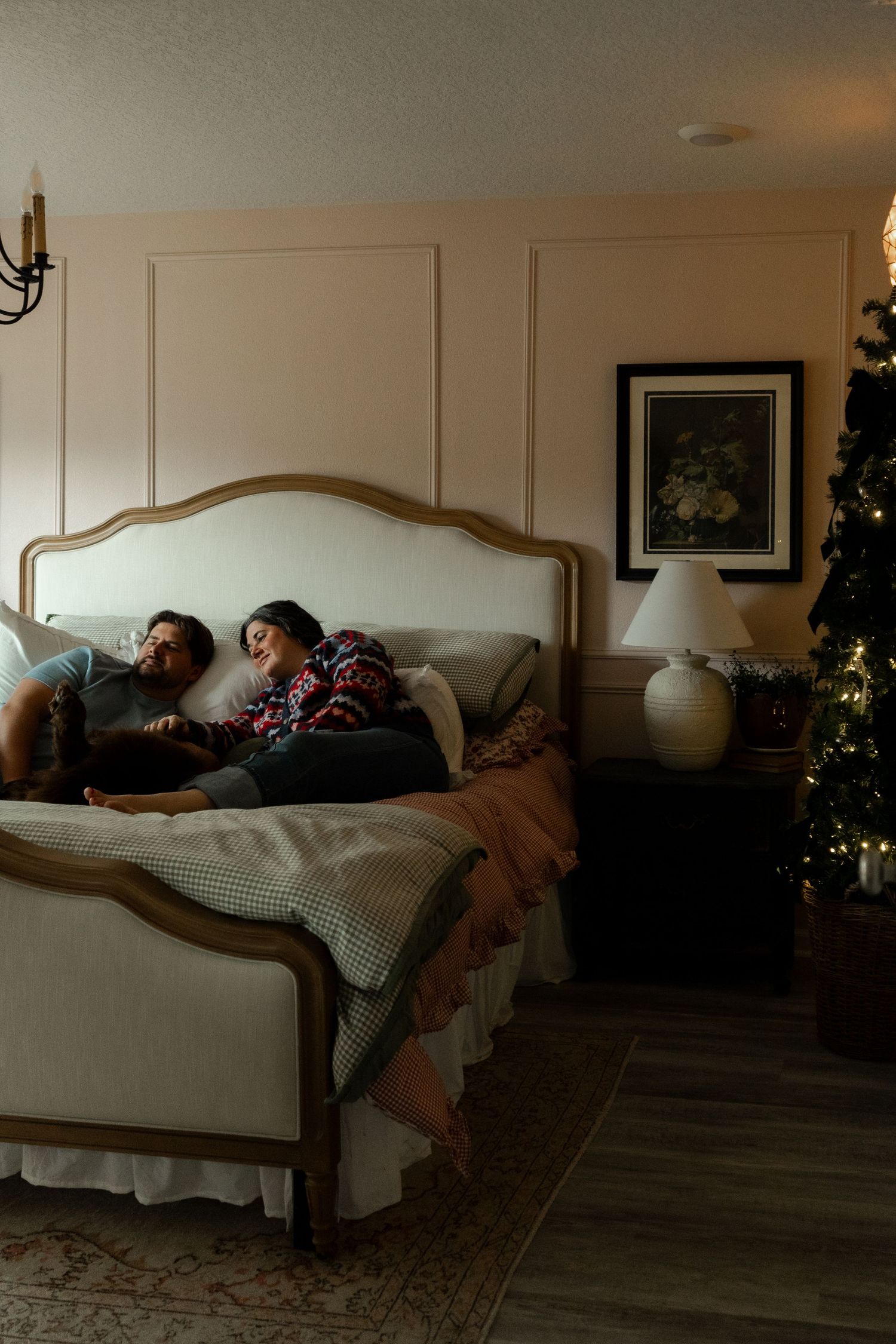 Couple relaxing on elegant bed in cozy Christmas bedroom with decorated tree and warm lighting.