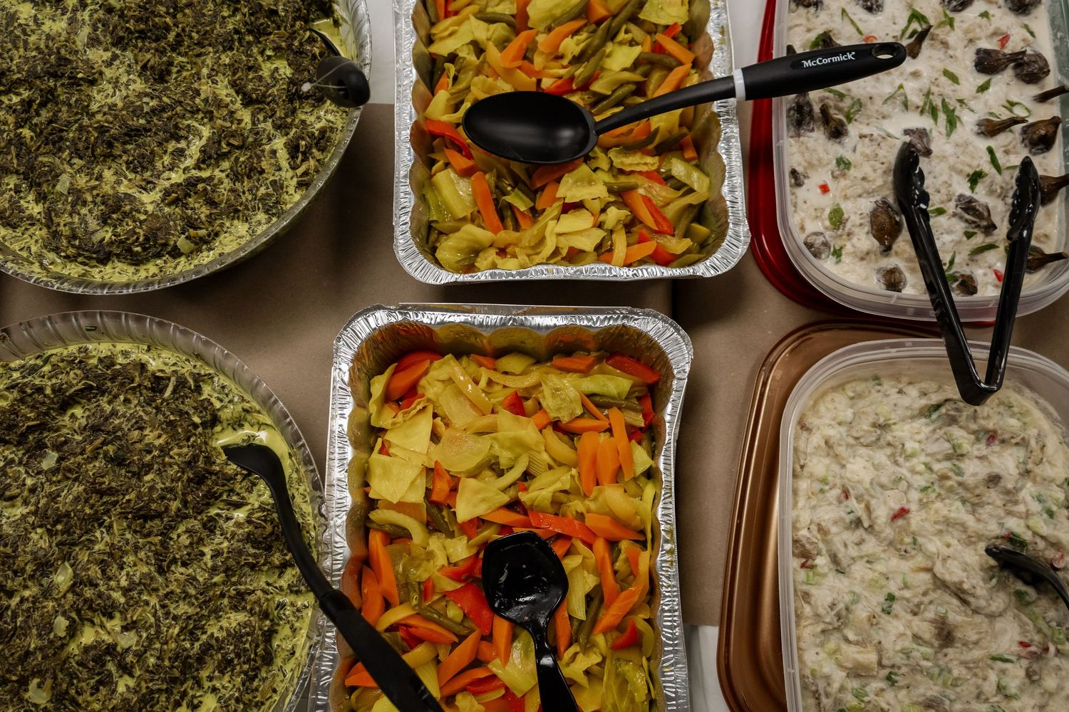Assorted traditional dishes including vegetables and salads displayed in aluminum trays.